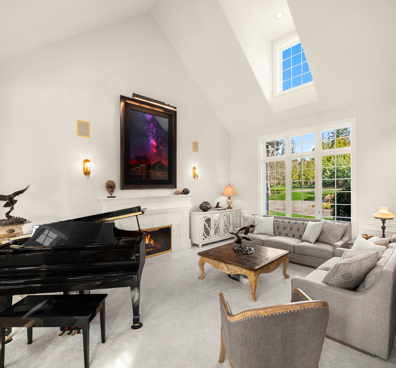 This is a spacious living room featuring high ceilings and large windows that provide ample natural light. The room is furnished with a grand piano, a fireplace, and comfortable seating arrangements, creating an elegant and inviting atmosphere. The decor is sophisticated, with a mix of classic and contemporary elements.