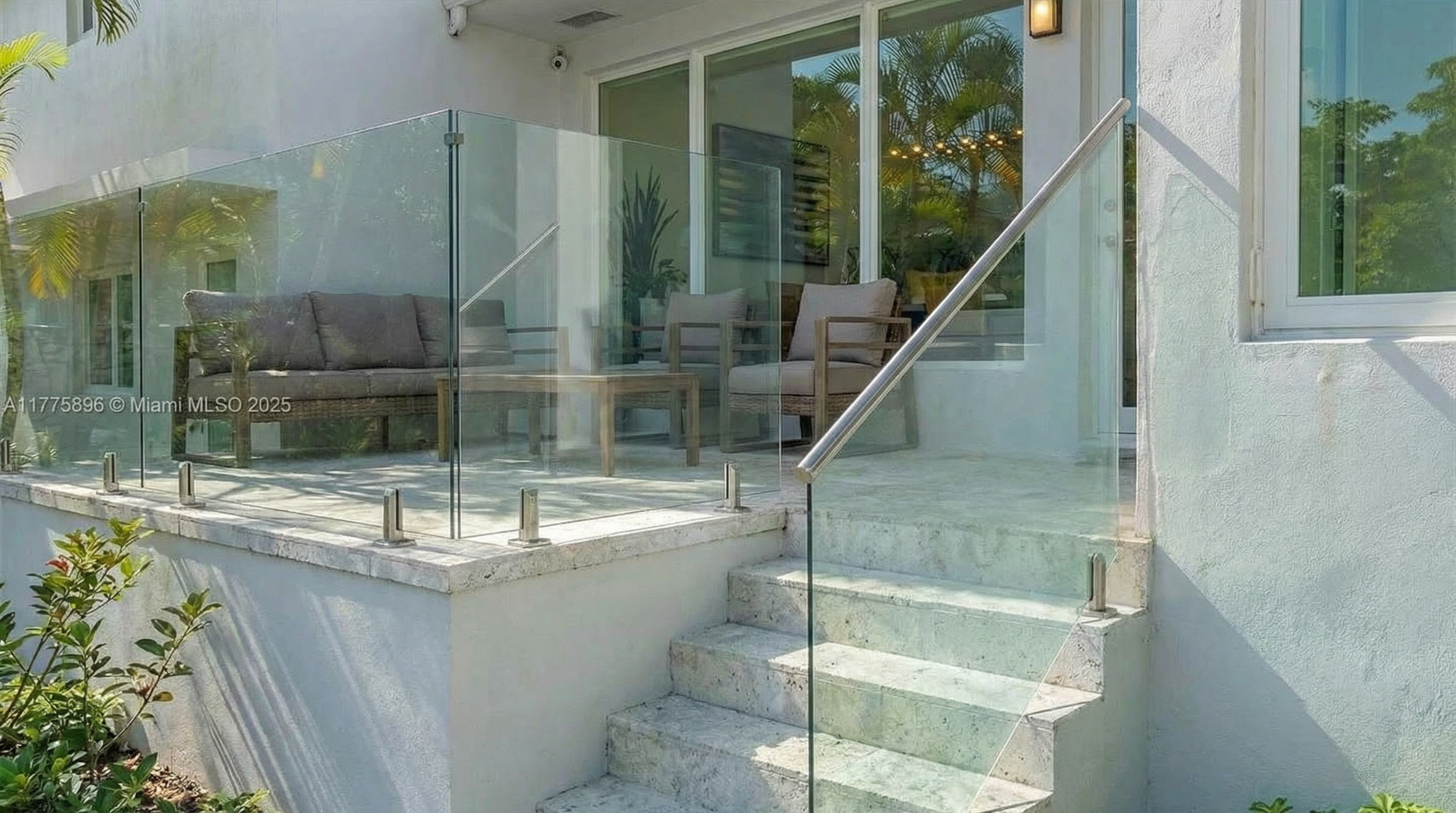 This image showcases a patio or balcony area of a property. It features modern glass railings and tiled steps. The scene includes outdoor furniture, suggesting a comfortable space for relaxation and entertainment.