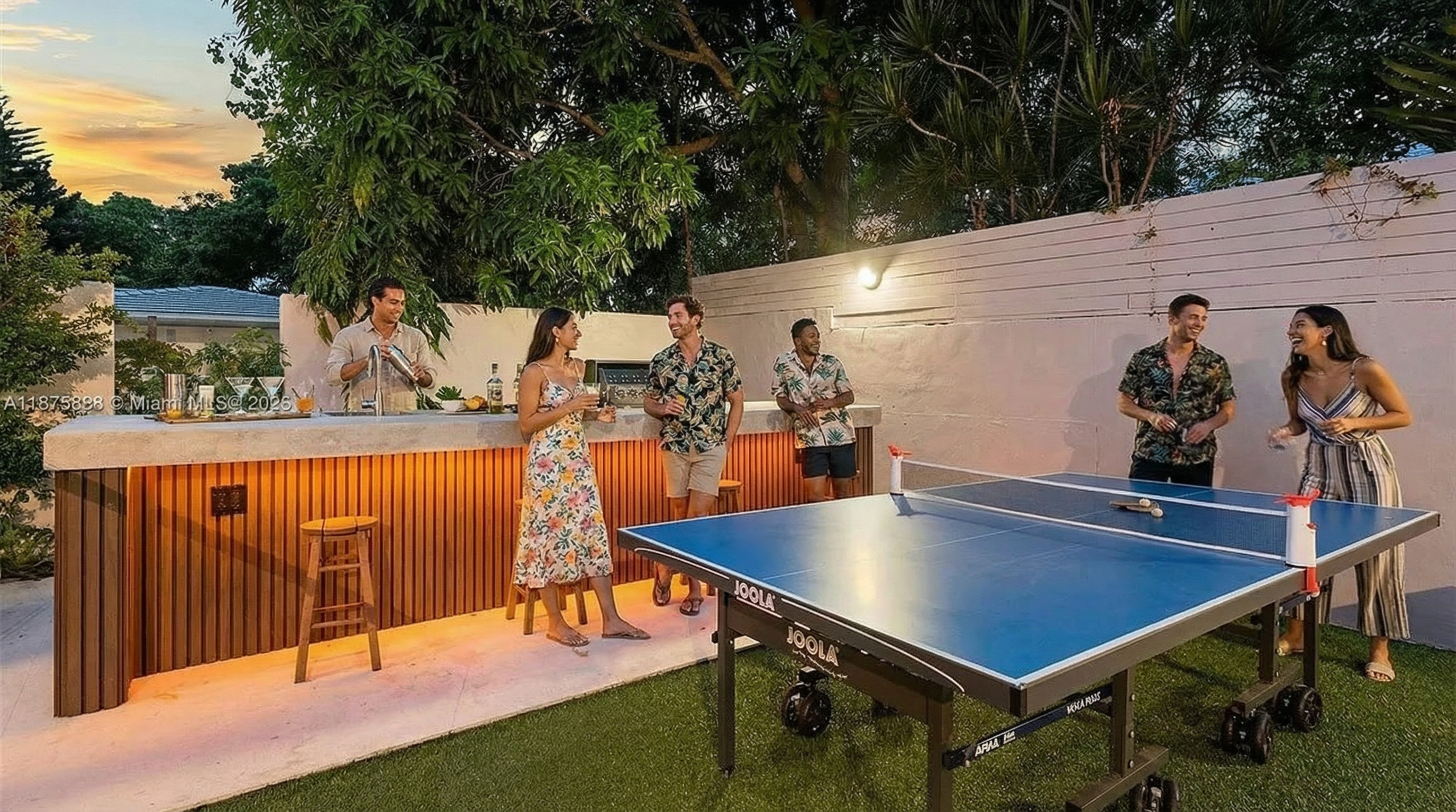 This outdoor space features an entertainment area complete with a bar and a ping pong table, perfect for hosting gatherings. The background features lush greenery and a neatly kept fence, creating a private and inviting atmosphere. The scene suggests a relaxed and social ambiance, enhancing the property's appeal.