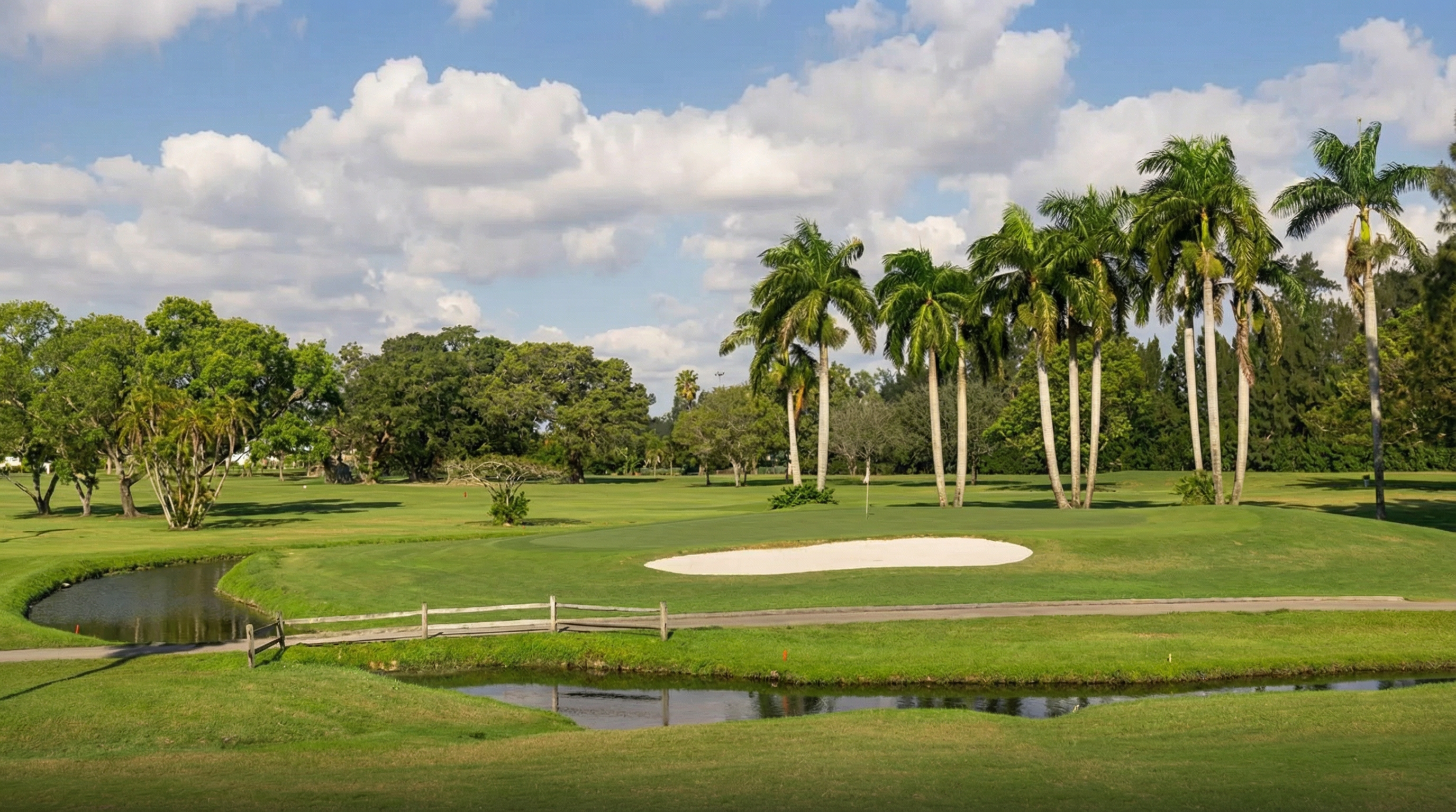 This image showcases a well-maintained golf course, a desirable community amenity. The manicured green, sand trap, and mature palm trees enhance the property's appeal. A small wooden bridge crosses a water feature, adding to the course's scenic charm.
