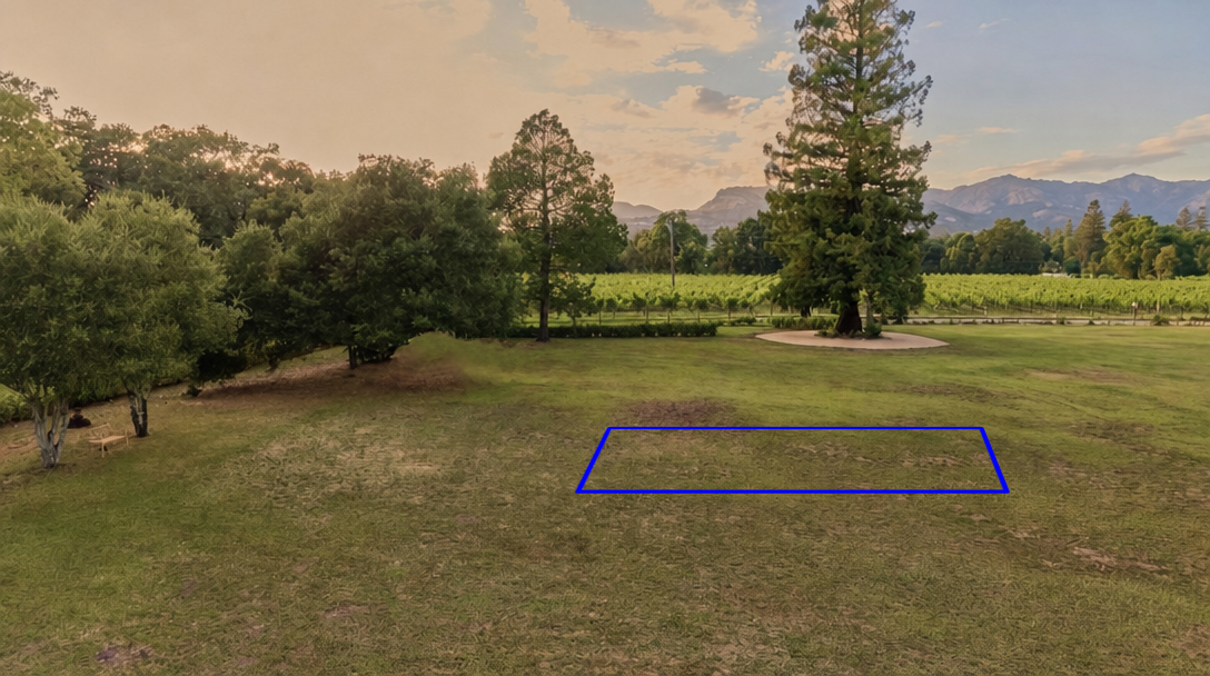 This spacious, open lawn area features lush green grass with mature trees and a scenic vineyard in the background. The landscape is framed by distant mountains, emphasizing a tranquil, picturesque setting suitable for outdoor activities or potential development. A blue rectangular outline highlights a specific portion of the yard, suggesting a designated spot for a future structure or landscaping feature.