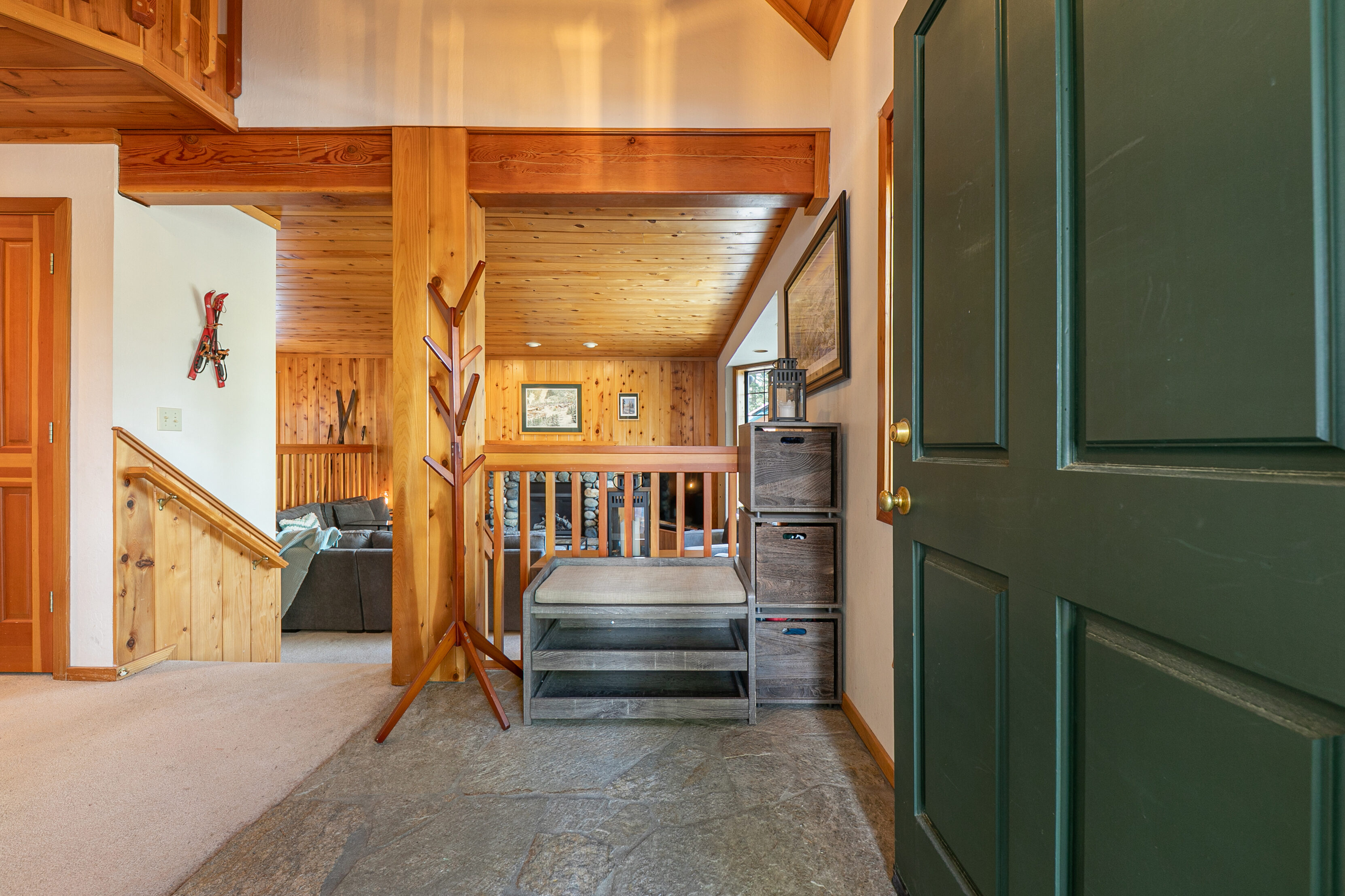 This rustic entryway features charming wood plank walls and ceilings, complemented by a durable stone floor. The space includes a convenient coat rack, a built-in bench with storage cubes, and clear sightlines into the cozy living area, creating a warm and inviting first impression.