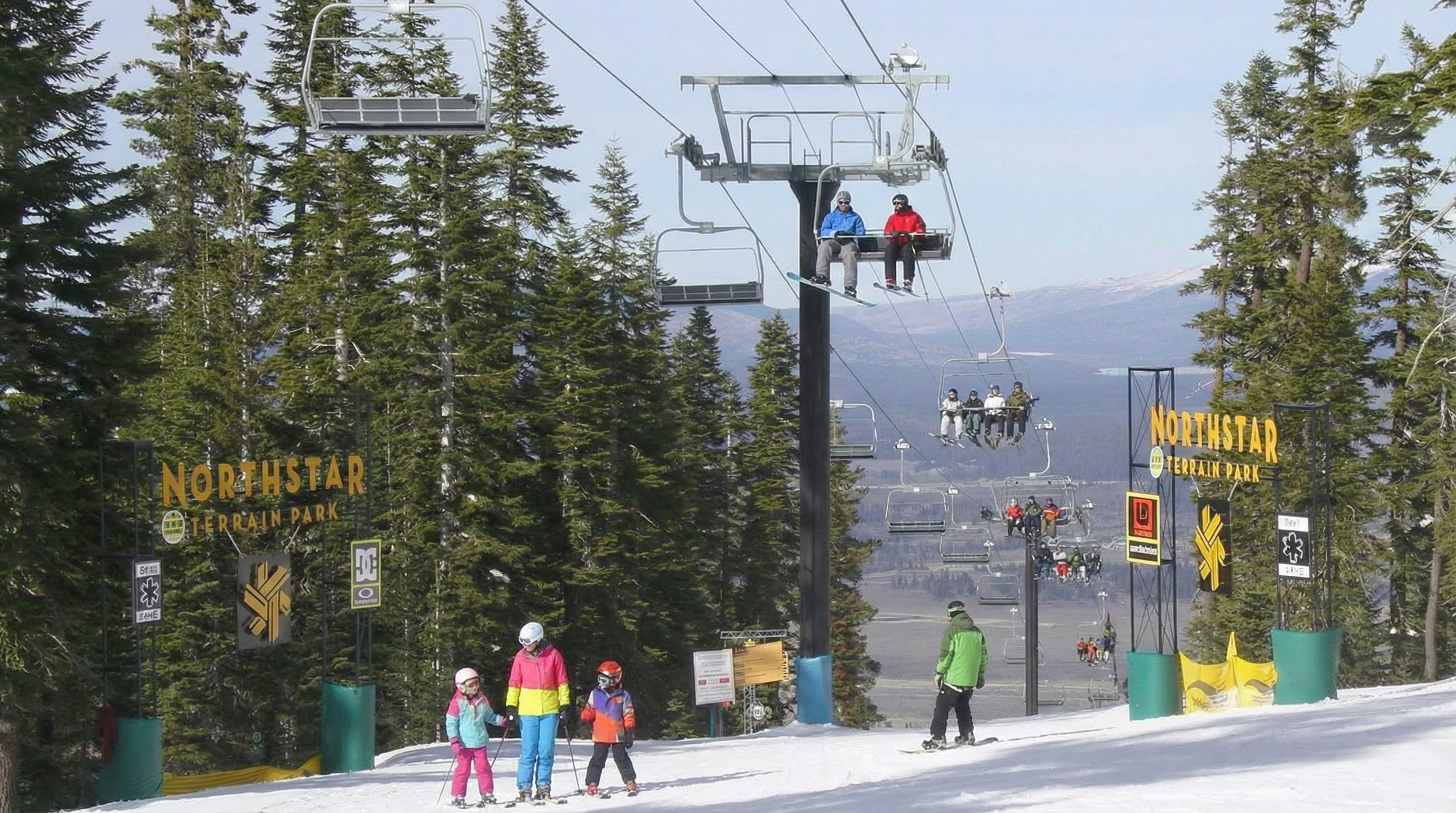 The image showcases the Northstar Terrain Park, a winter sports amenity. Ski lifts transport skiers and snowboarders up the mountain, and signage indicates the park's name. The scene suggests a recreational environment suitable for families and winter sports enthusiasts.