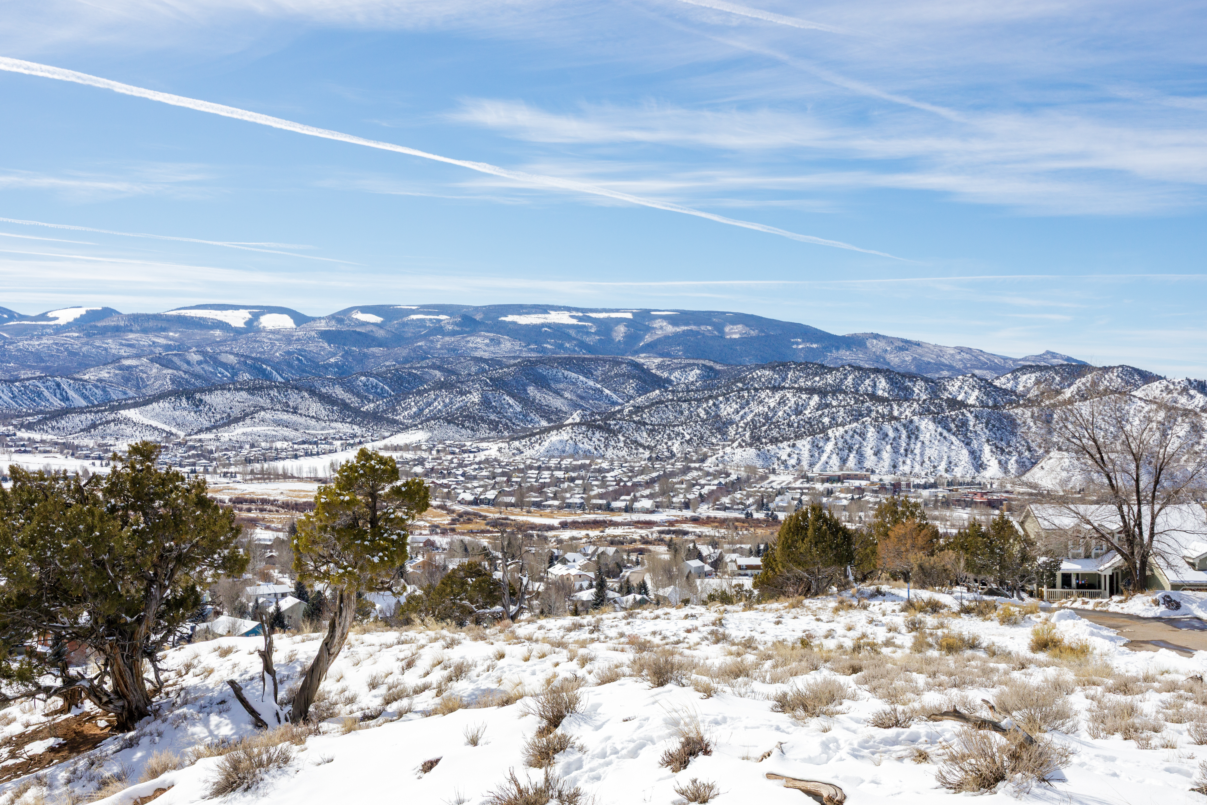 This image showcases an elevated view of a residential area nestled within a mountainous landscape. The houses display diverse architectural styles, all lightly dusted with snow, integrating seamlessly with the winter scenery. This vista emphasizes the serenity and picturesque beauty of the location, highlighting its appeal for those seeking a tranquil environment with scenic views