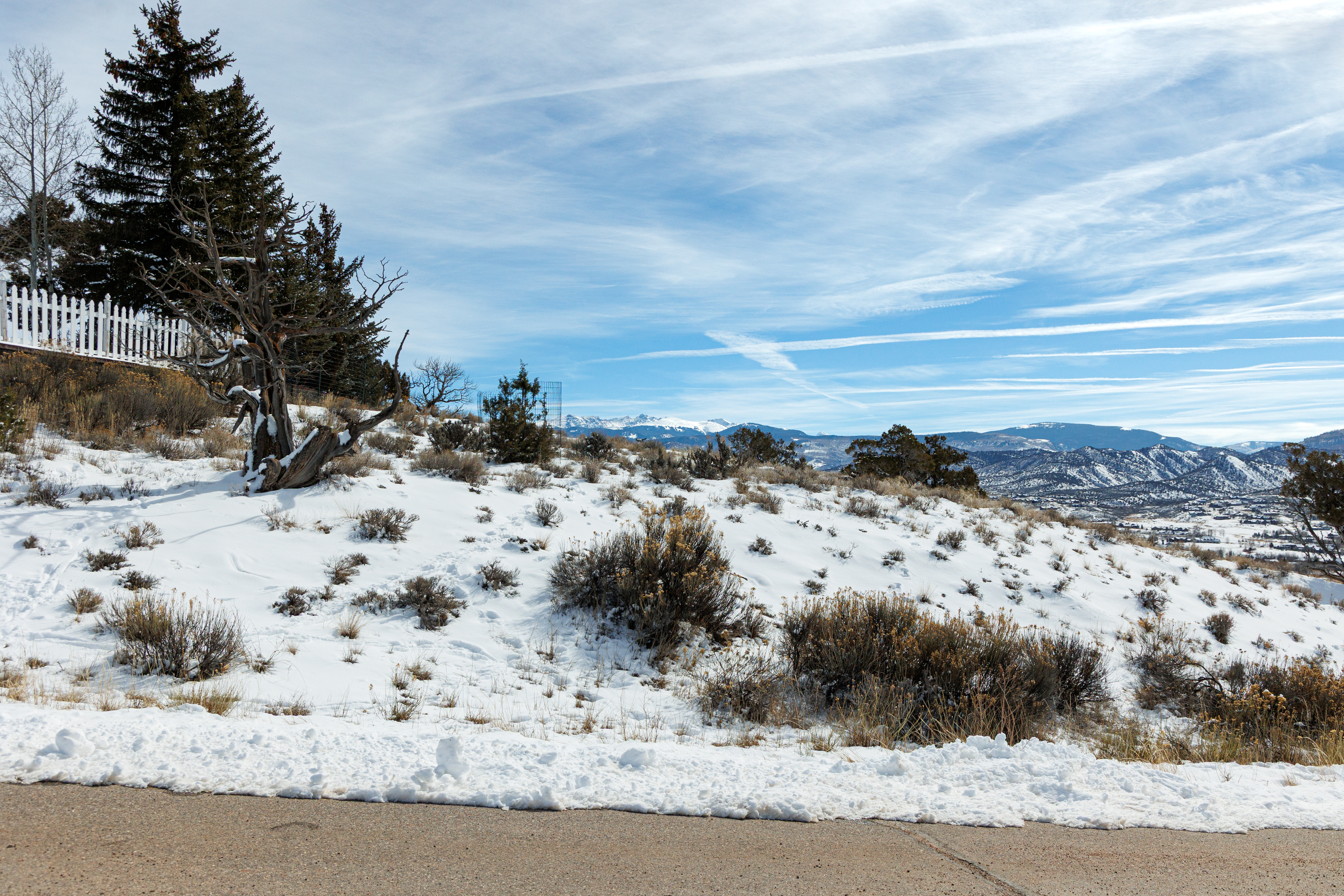 This image showcases a snowy landscape with a clear view of distant mountains, potentially highlighting a property's scenic surroundings. The presence of mature trees and natural vegetation add to the appeal of the outdoor space. The road in the foreground suggests easy access and connectivity.