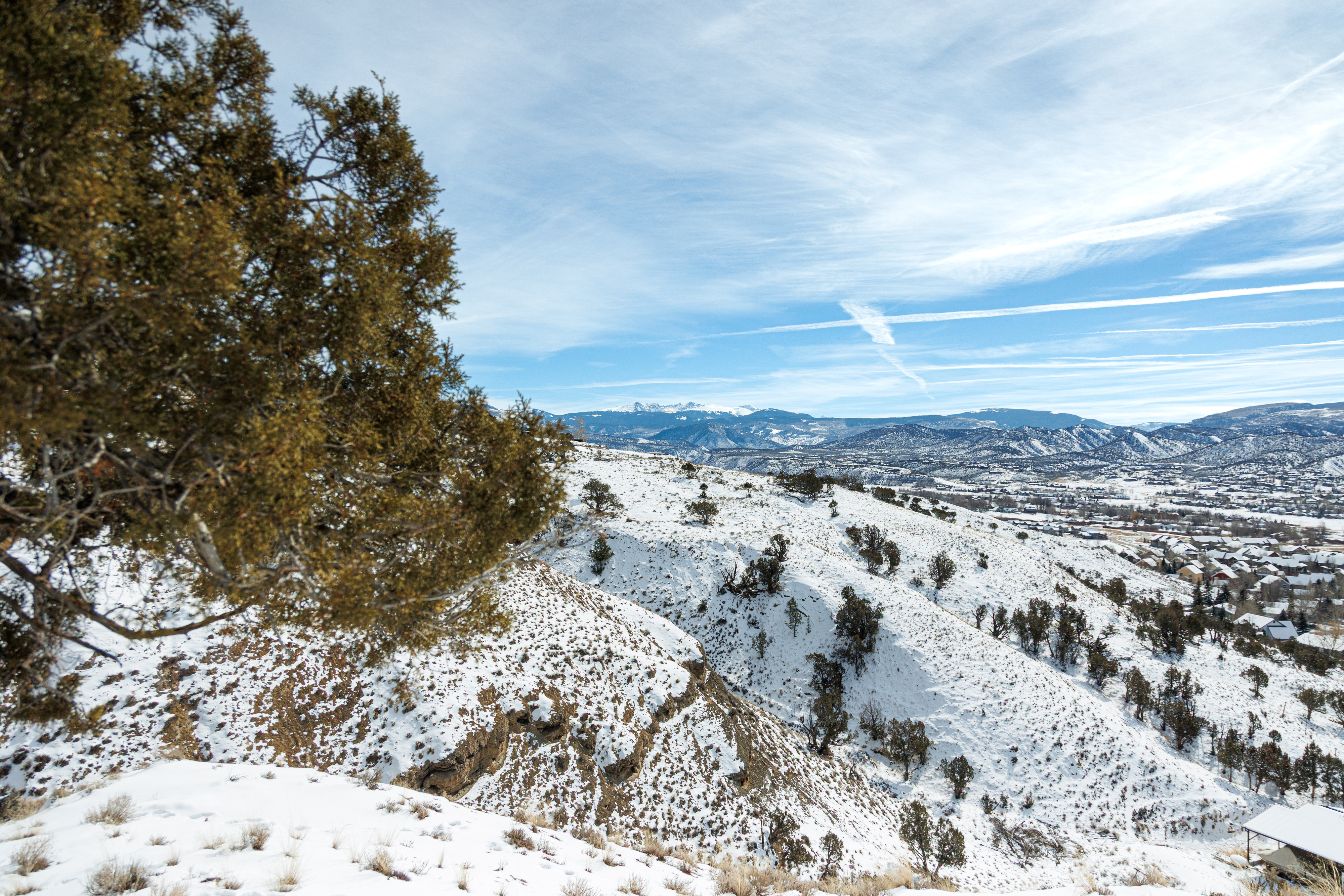 This aerial shot depicts a snowy landscape featuring mountain ranges and a valley with scattered residential properties. The foreground showcases a snow-covered hillside with some vegetation. The image would highlight the natural beauty and potential for outdoor activities associated with the property's location.