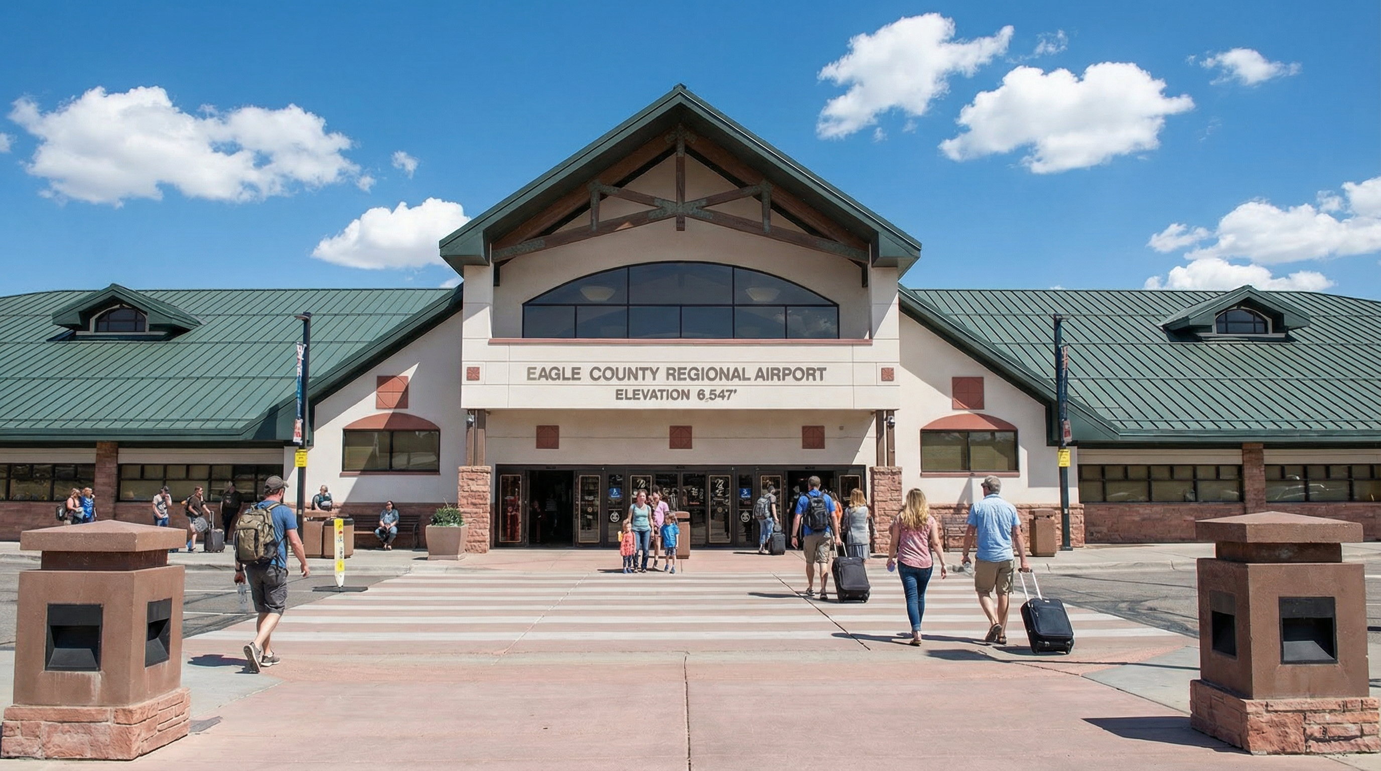 The image showcases the front exterior of the Eagle County Regional Airport. The building has a symmetrical design with a peaked central section and lower wings on each side. A clearly marked crosswalk leads to the entrance, adding to the accessibility and welcoming appearance.