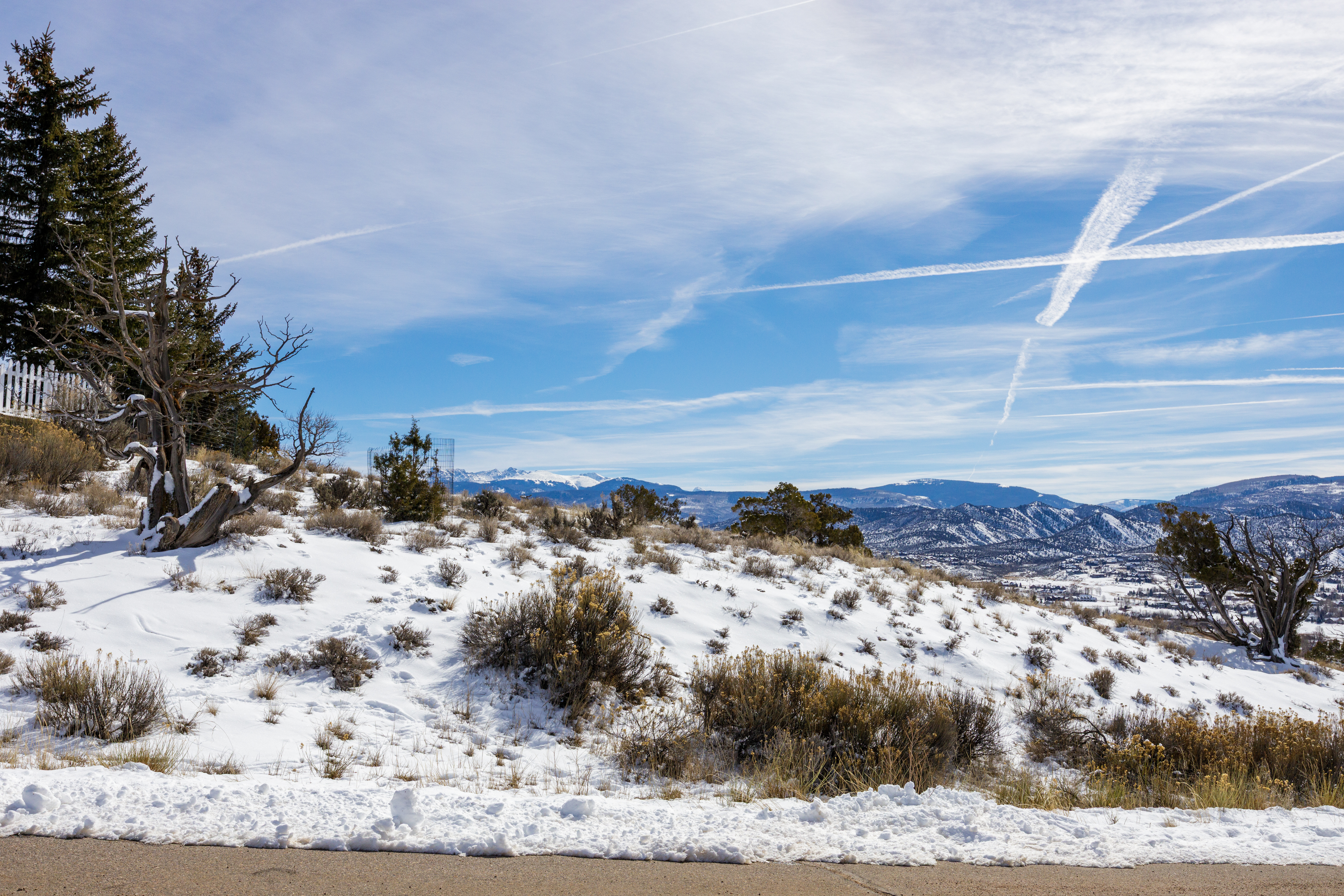 This exterior image offers a side view of a property set against a scenic backdrop. The landscape is covered in snow, lending a wintry charm. A paved road runs in front of the snowy hillside, showcasing the accessibility of the location with mountains in the distance.