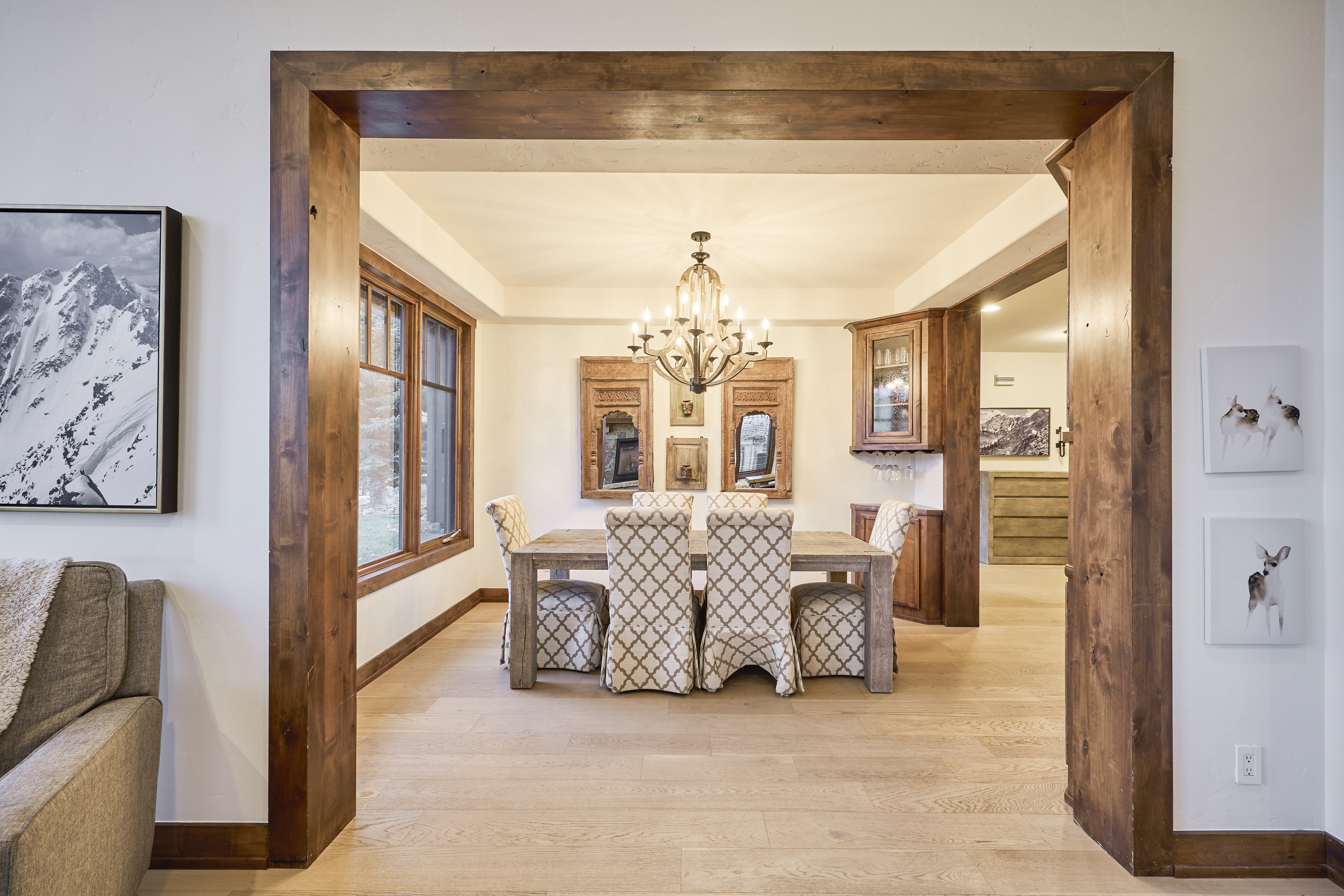 This inviting dining room features a rustic wood dining table and upholstered chairs. A decorative chandelier hangs above, and natural light streams in through a nearby window. The space exudes a warm, elegant ambiance, perfect for family gatherings and entertaining.