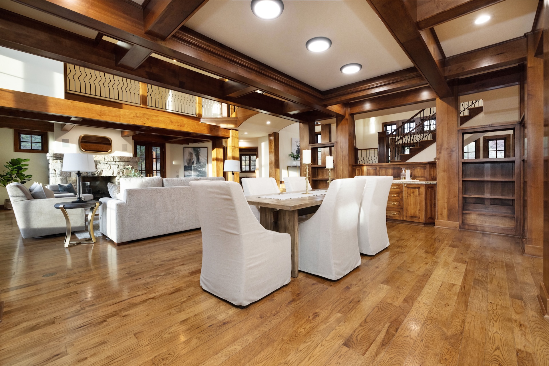 This interior shot showcases a dining room with a rustic, yet elegant appeal. The room features a wooden table surrounded by white upholstered chairs set on hardwood flooring. Exposed wooden beams along the ceiling add character, complementing the warm, inviting atmosphere perfect for family gatherings and formal dinners.