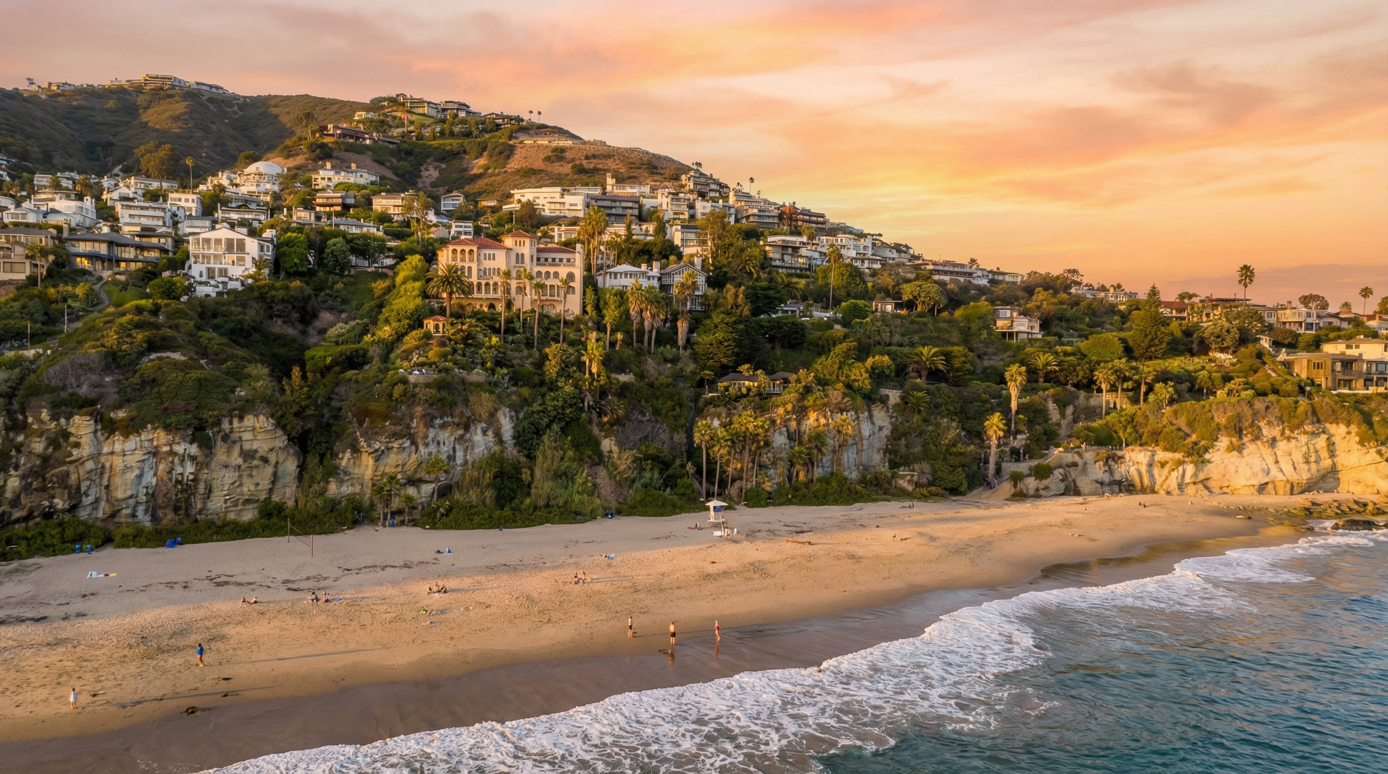 This aerial view showcases an impressive coastal property with stunning sunset lighting. The image highlights the hillside houses, lush landscaping, and its direct beach access with ocean views. The property offers private coastal living with an appealing blend of nature and luxury.