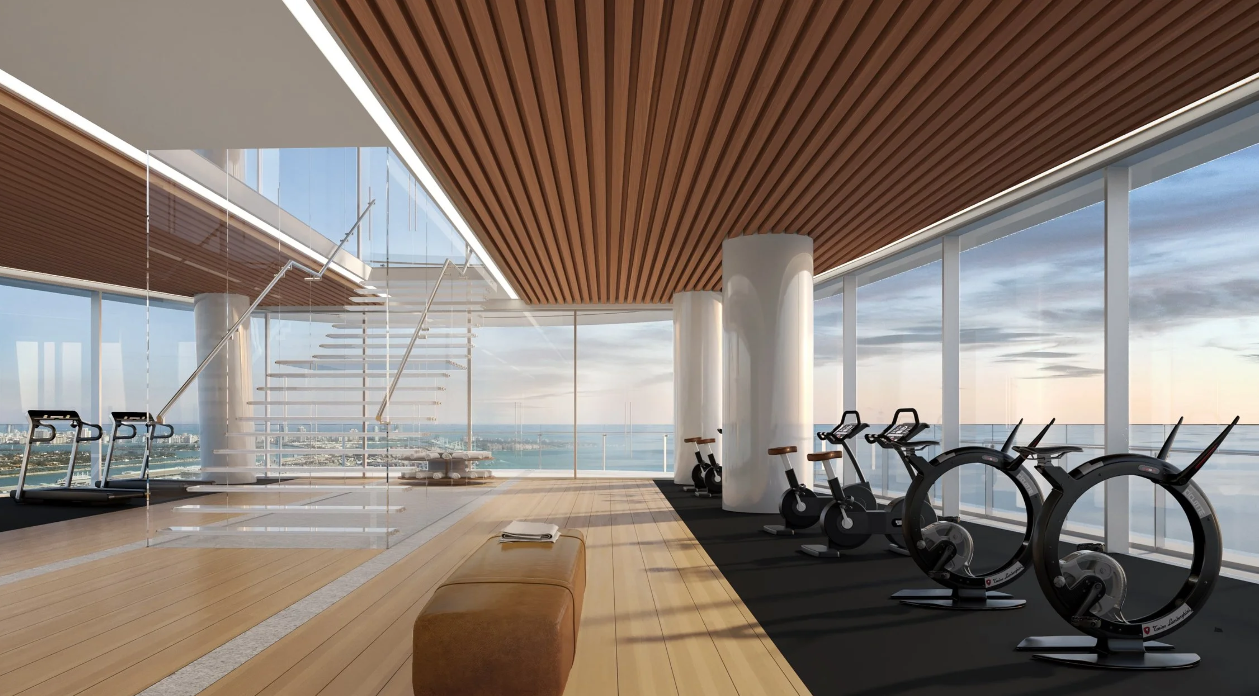This modern home gym boasts floor-to-ceiling windows offering panoramic views. The space is well-equipped with state-of-the-art exercise equipment, including treadmills and stationary bikes. Wood floors add warmth, complemented by the sleek black mats under the cardio machines.