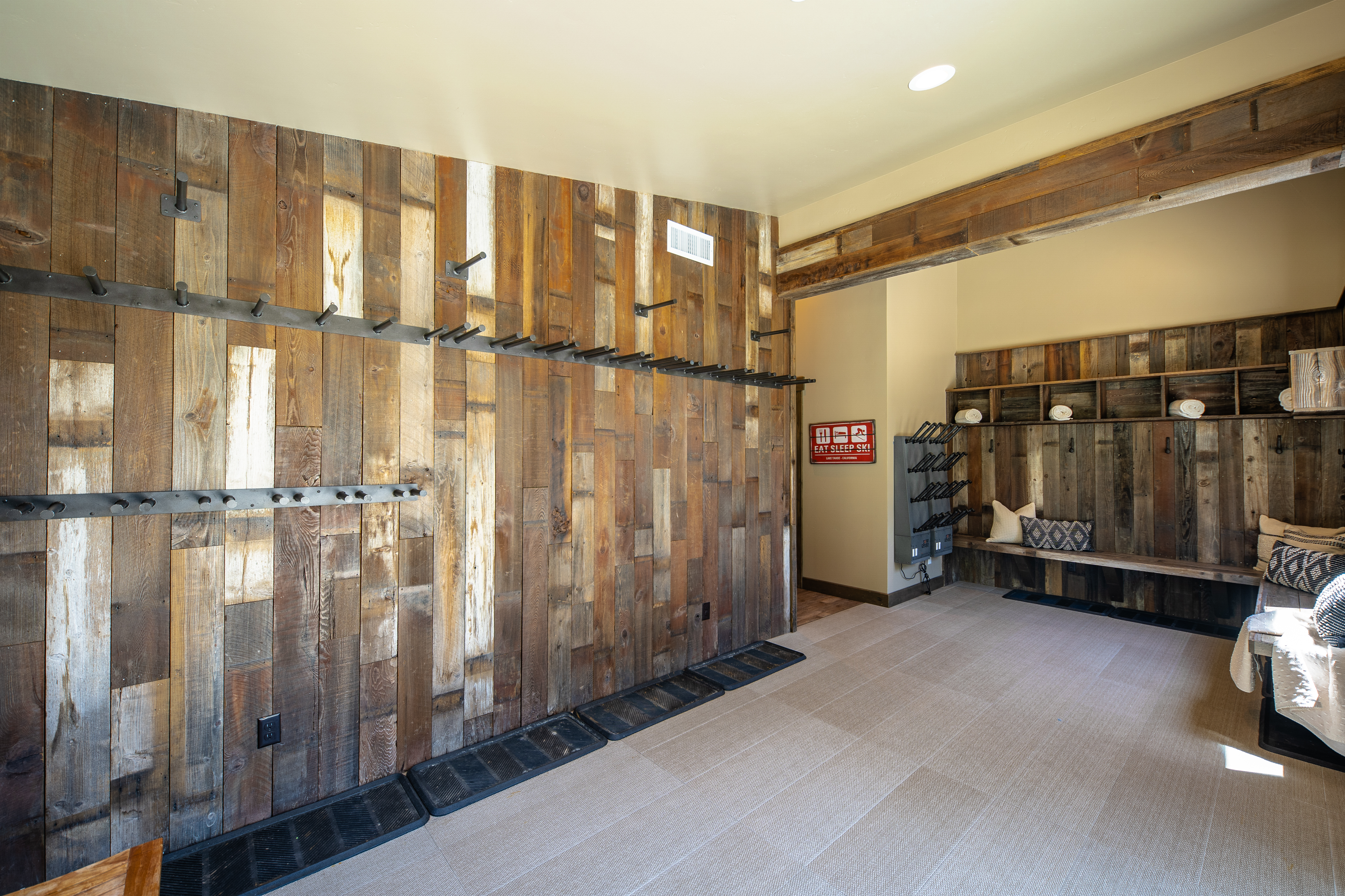 The image showcases an interior hallway or entryway with a rustic, lodge-style design. The walls are covered in reclaimed wood, accented by metal coat racks. A built-in bench and shelving unit offer storage and seating, contributing to the warm and inviting atmosphere.