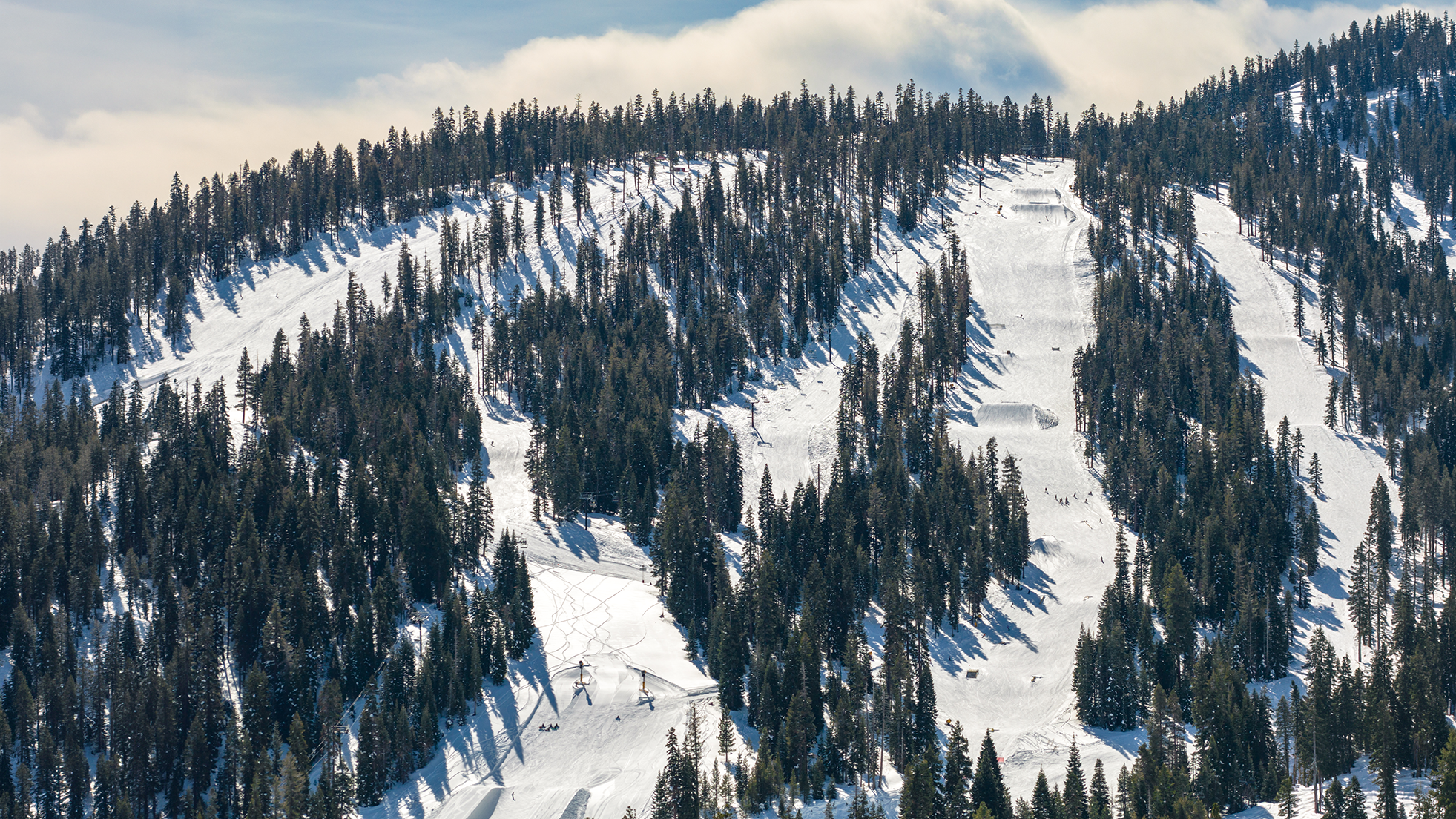 The image depicts a ski resort amenity: ski slopes densely surrounded by evergreen trees. The slopes are covered in snow and show signs of use from skiers/snowboarders. This highlights recreational opportunities at the location.