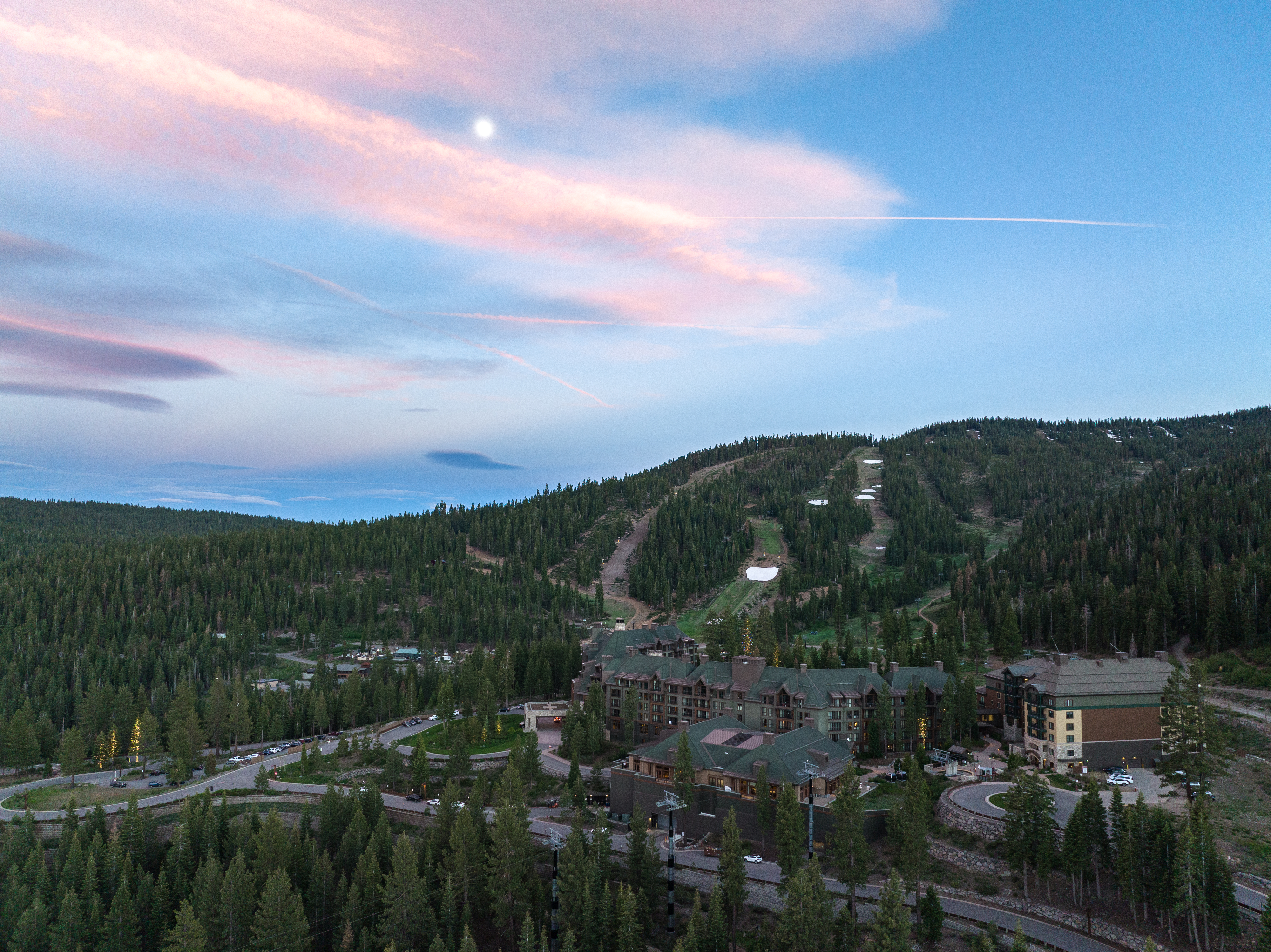 This aerial view showcases a luxurious resort nestled within a mountain landscape. The building's architecture blends seamlessly with the natural environment. Ski slopes are visible in the background, suggesting a desirable location for outdoor enthusiasts and a potential for year-round activities.