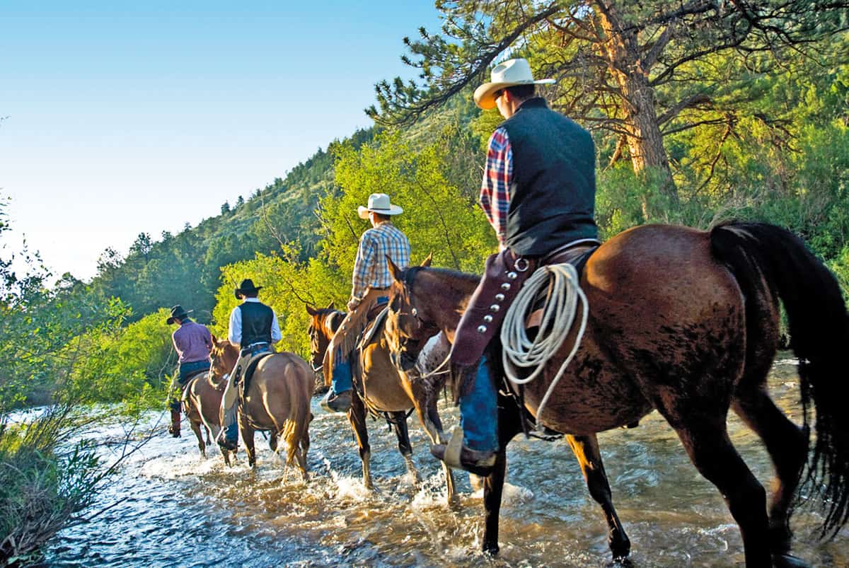 This image showcases a group of horseback riders crossing a shallow river, set against a backdrop of lush greenery and a tree-covered hillside. The scene evokes a sense of outdoor adventure and recreational opportunity, which could be related to real estate near trails or equestrian facilities. The natural setting enhances the property's appeal for buyers interested in a rural or outdoor lifestyle.