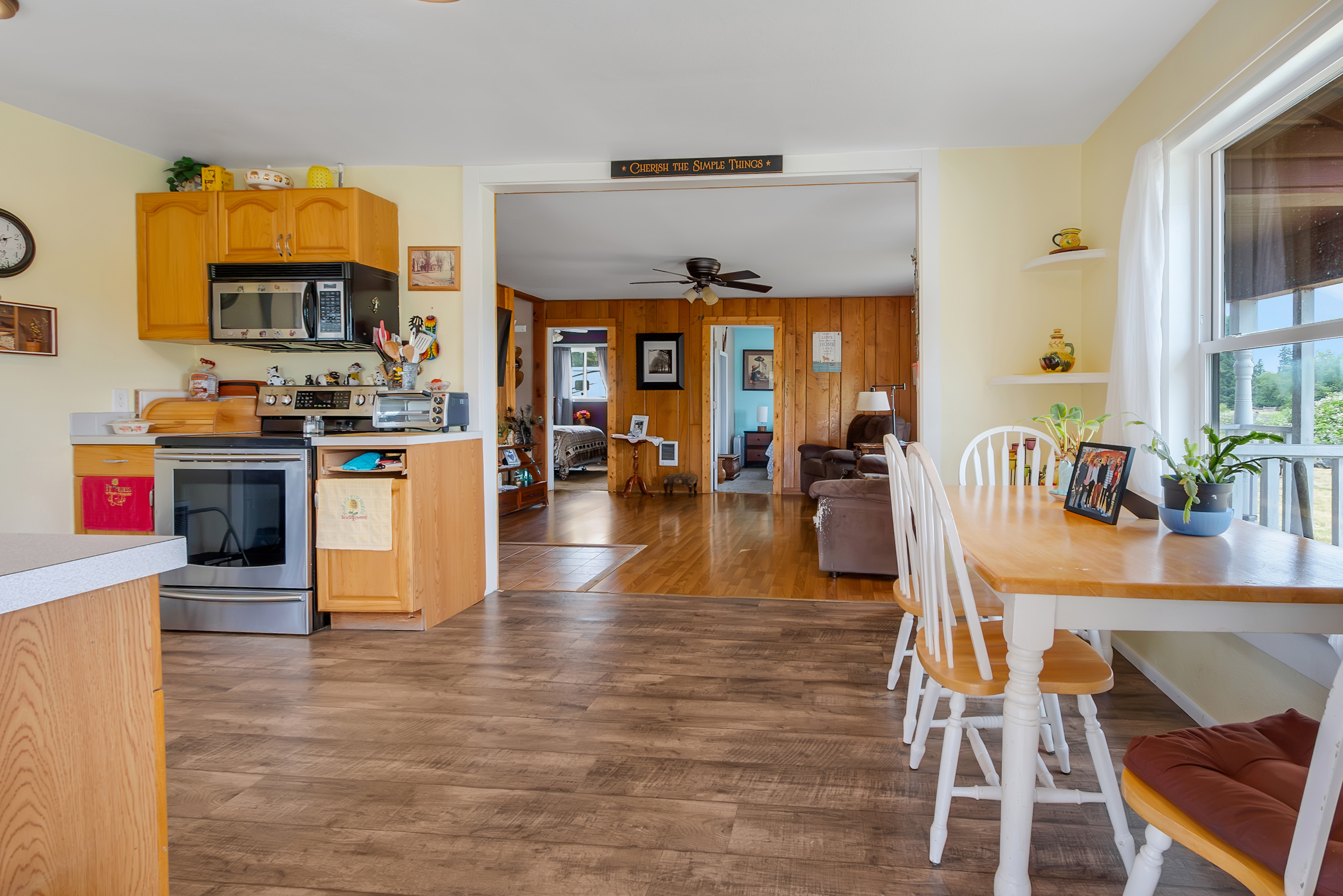 This interior shot showcases a cozy kitchen that flows into a living area. The kitchen features wooden cabinets, stainless steel appliances, and a countertop with various kitchen items. The living area has wood-paneled walls and comfortable seating, creating a warm and inviting atmosphere.
