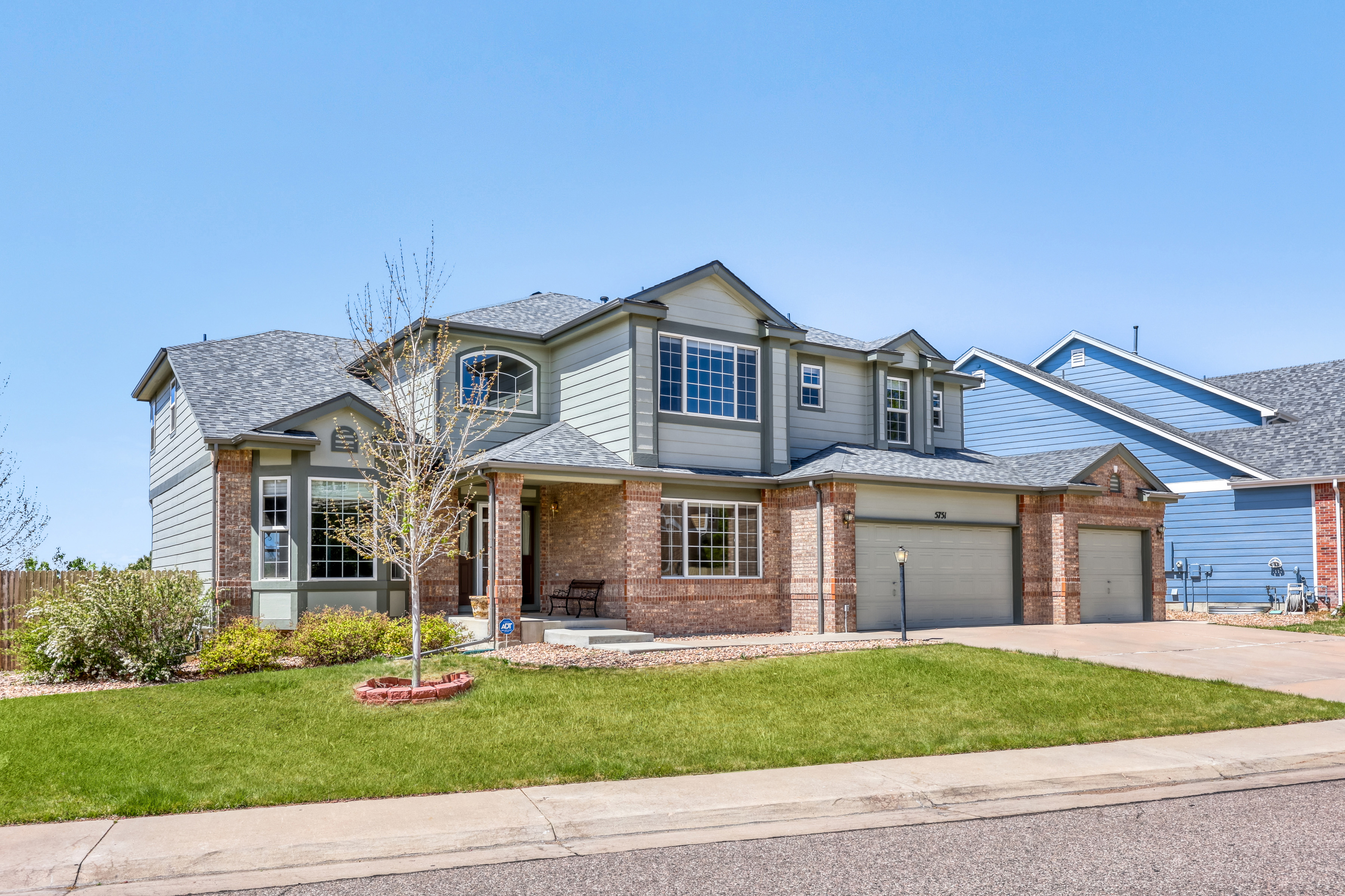 This is a two-story single-family home with a classic brick and siding exterior and an attached three-car garage. The front of the house features a welcoming covered entryway, large windows that allow for natural light, and a neatly manicured lawn with mature landscaping. It presents a traditional and well-maintained appearance, typical of a modern suburban residential neighborhood.