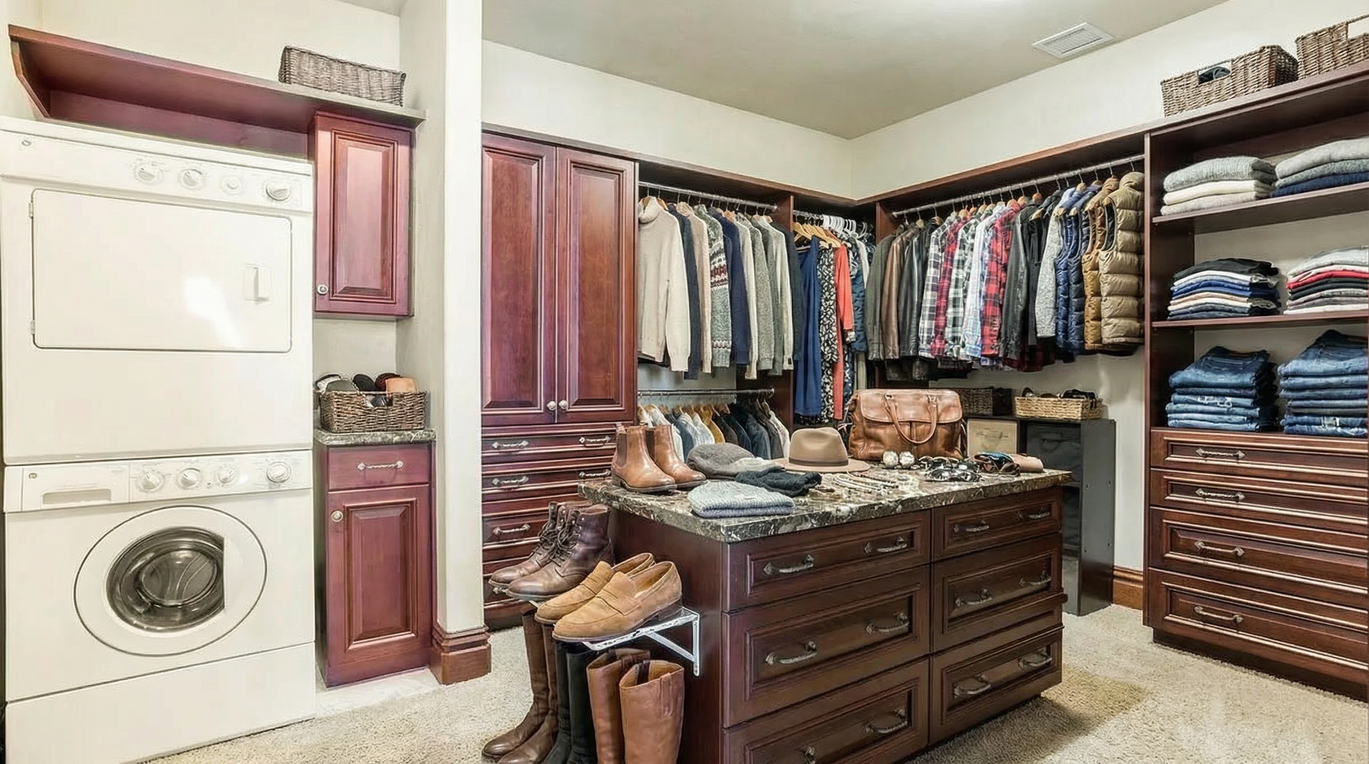 This is a well-organized walk-in closet featuring custom cabinetry and ample storage space. The closet includes hanging rods for clothes, shelving for folded items, and drawers for smaller accessories. A central island provides a surface for laying out outfits and includes additional storage below.