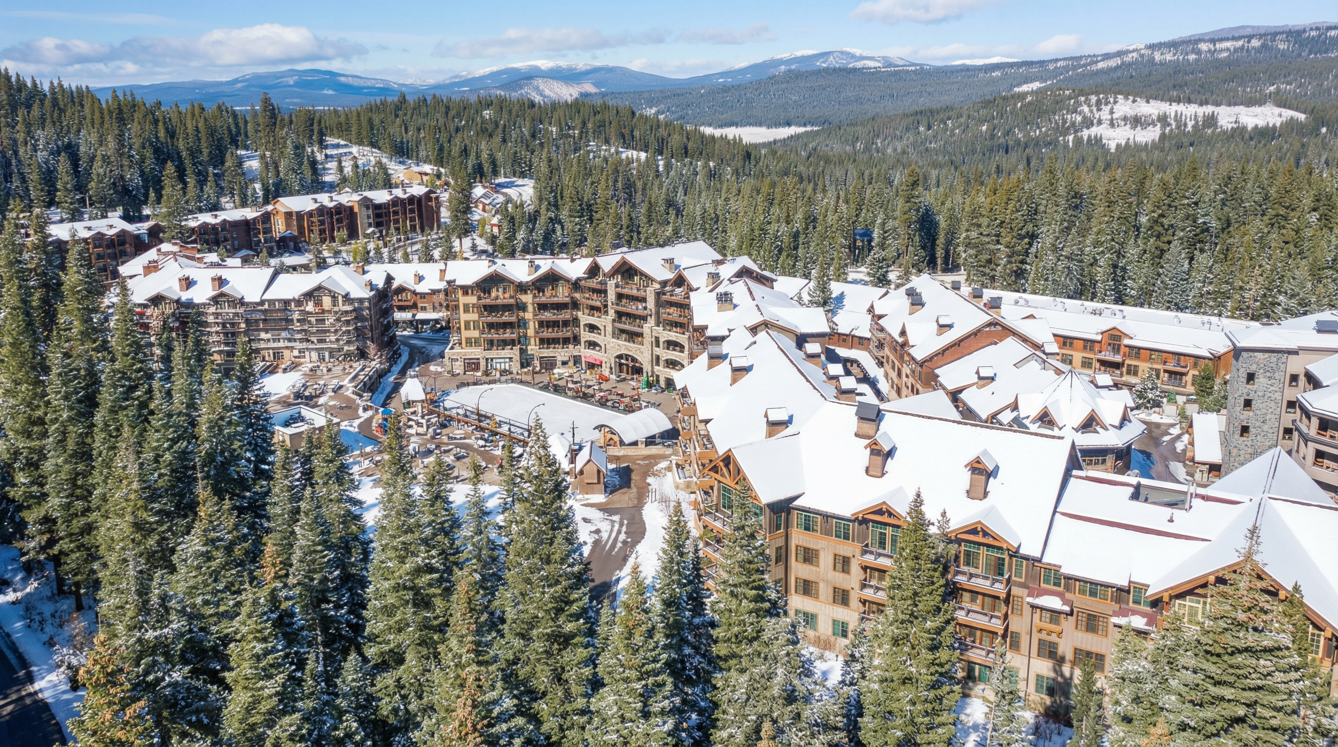 This aerial view showcases a luxury resort nestled in a snow-covered mountain landscape. The architecture features a mix of stonework and wood, with multiple balconies offering stunning views. The surrounding evergreen trees add to the serene and secluded atmosphere, making it an attractive property for those seeking a winter retreat.