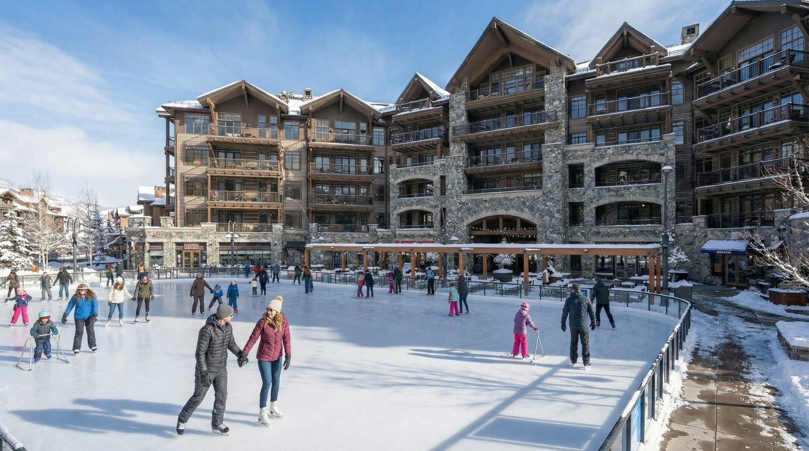 This image showcases an outdoor ice skating rink surrounded by a multi-story, stone and wood finished building, likely a resort or condominium complex. The rink is actively in use by families and individuals, adding a lively atmosphere to the scene. The surrounding architecture, combined with the icy landscape, suggests a desirable location for winter recreation and community engagement.