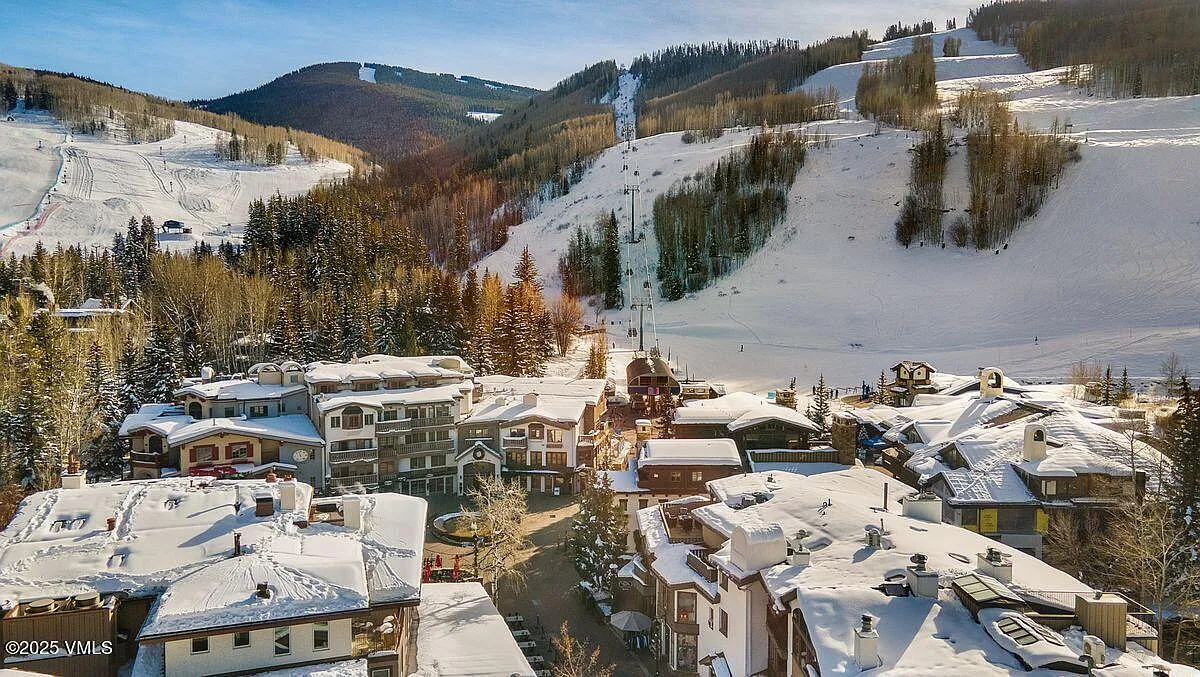 This aerial view showcases a luxury ski resort community amidst a snowy mountain landscape. The roofs of the buildings are covered in snow, suggesting a winter setting. A ski lift is visible on the mountainside, emphasizing the property's convenient access to winter sports activities.