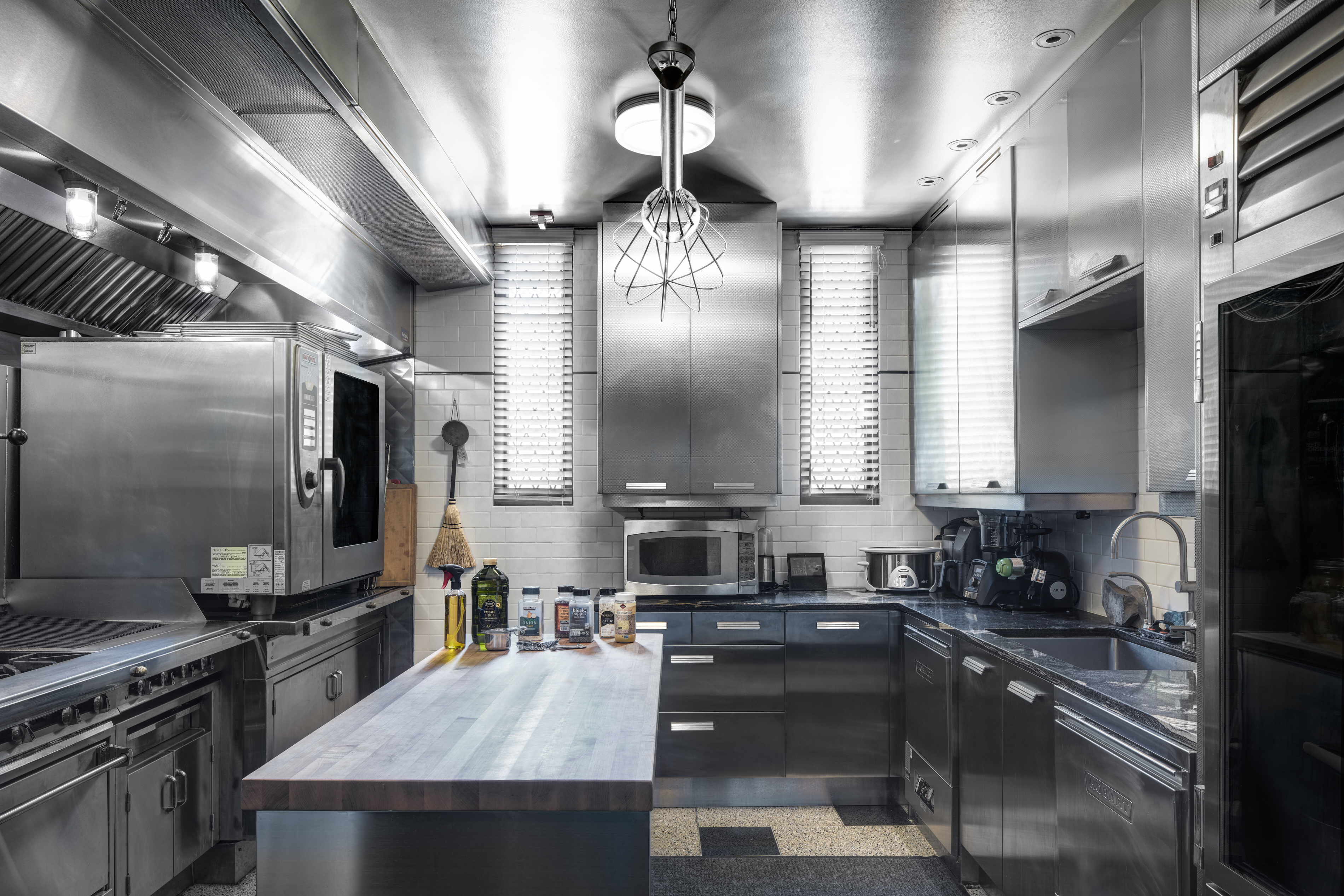 This is a professional-grade kitchen featuring stainless steel cabinetry, appliances, and countertops. A butcher block island provides ample workspace, while a commercial oven and range offer high-end cooking capabilities. The space is well-lit and designed for efficiency, making it ideal for serious cooking enthusiasts.