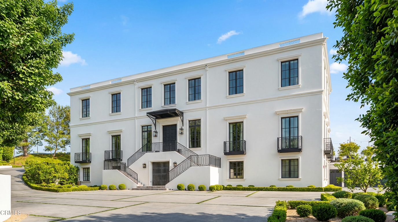 The image showcases the front exterior of a grand, modern white residence. Key features include a prominent entrance staircase, symmetrical window placement with dark frames, and minimal landscaping with neatly trimmed shrubs. The overall impression is one of sophisticated elegance and stately curb appeal, suitable for a high-end real estate listing.