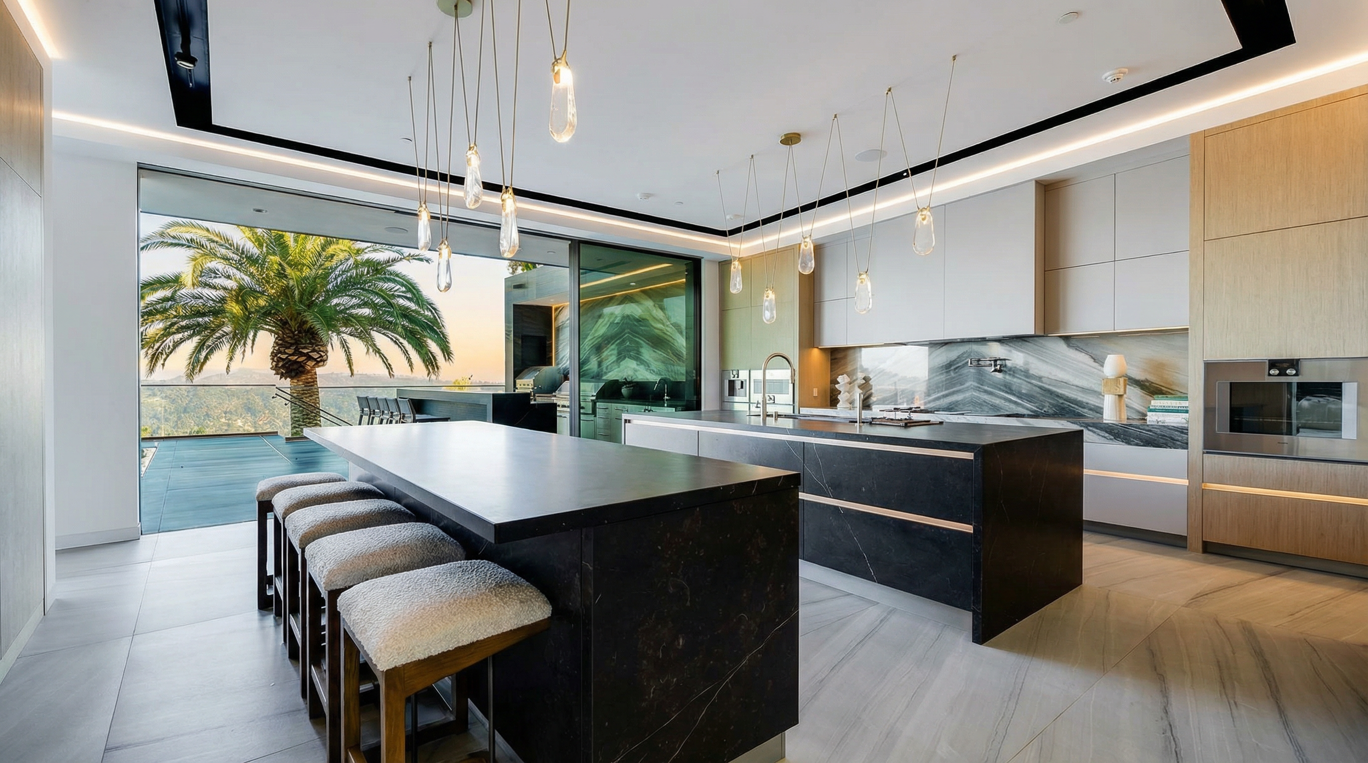 This is a modern, luxury kitchen featuring sleek cabinetry in light wood and white tones, paired with dark marble islands. The countertops are clean and expansive, providing ample workspace, and it boasts high-end appliances. Large sliding glass doors open to an outdoor area, offering a breathtaking view and creating a seamless indoor-outdoor living experience.