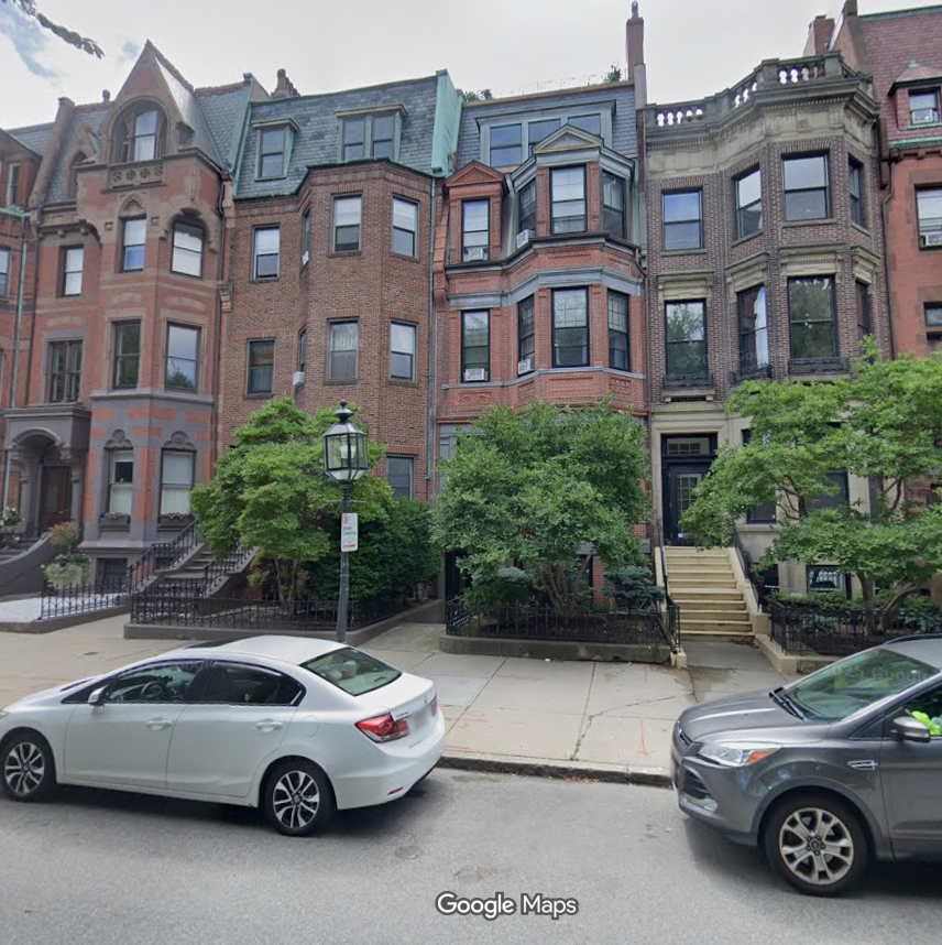 This image showcases a row of classic, historic brownstone or brick townhouses, likely in a city like Boston. The architectural style features ornate brickwork, tall windows, bay projections, and prominent entry staircases, exuding a high-end, traditional urban atmosphere. Mature trees and well-maintained iron fencing provide a picturesque and refined curb appeal for these multi-story residential properties.