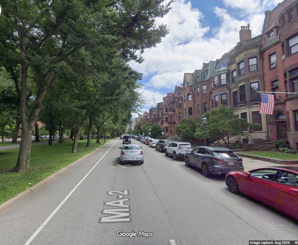 This image displays a quintessential street scene in Boston's historic Back Bay neighborhood, featuring iconic brownstone architecture and tree-lined sidewalks. The road is bordered by a well-maintained park on one side, showcasing an attractive urban environment with easy access to green space. The proximity of preserved historic residential buildings to public parkland highlights a desirable and upscale city location.