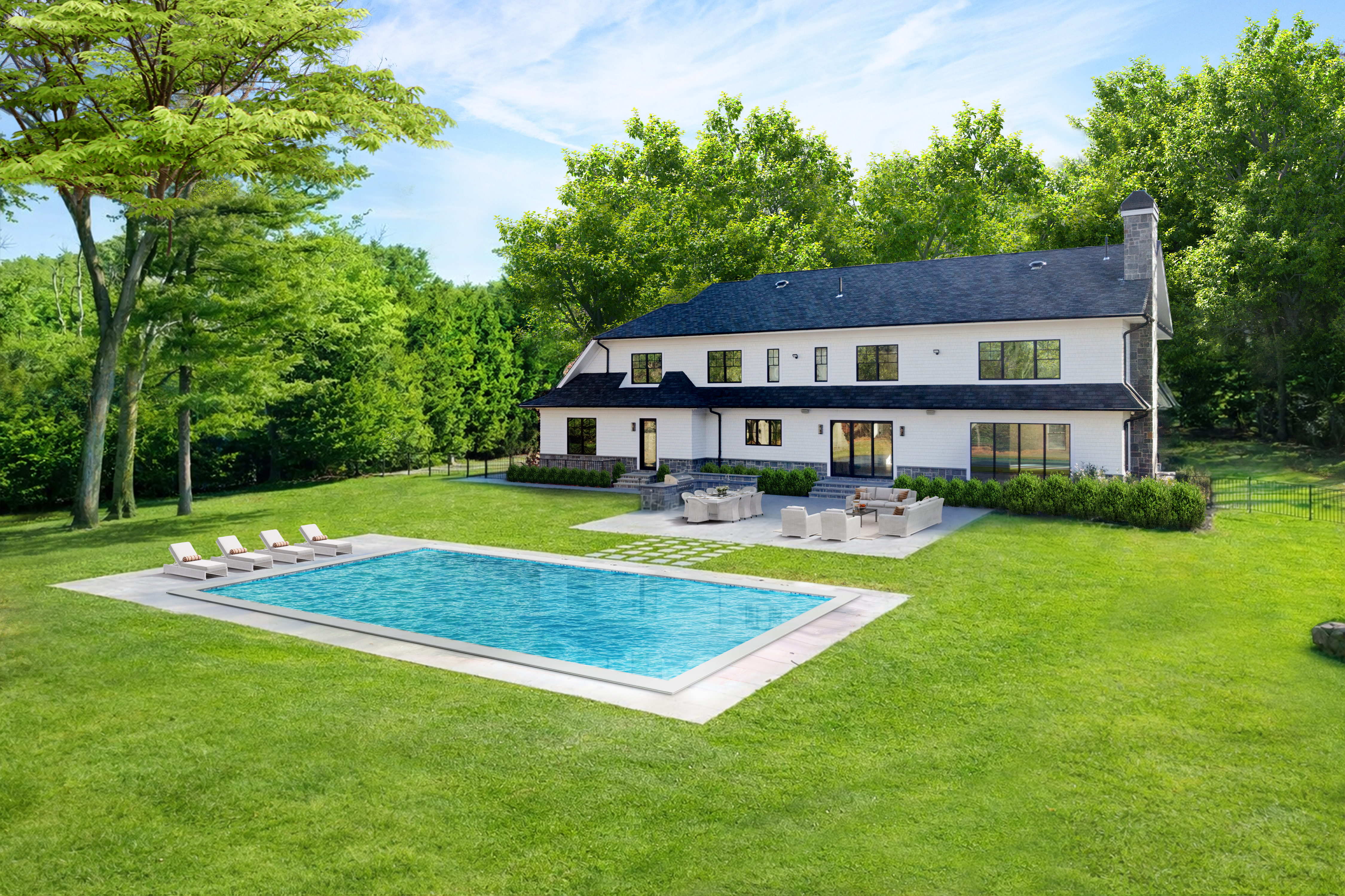 This expansive rear view of a luxury residence showcases a classic white-sided home with a dark shingled roof and stone accents. The property features a large, pristine rectangular swimming pool, a stone patio with outdoor seating, and a lush, manicured lawn surrounded by mature trees. The perspective is a wide-angle shot that captures the seamless integration of the home's architecture with its generous outdoor living and recreational spaces.