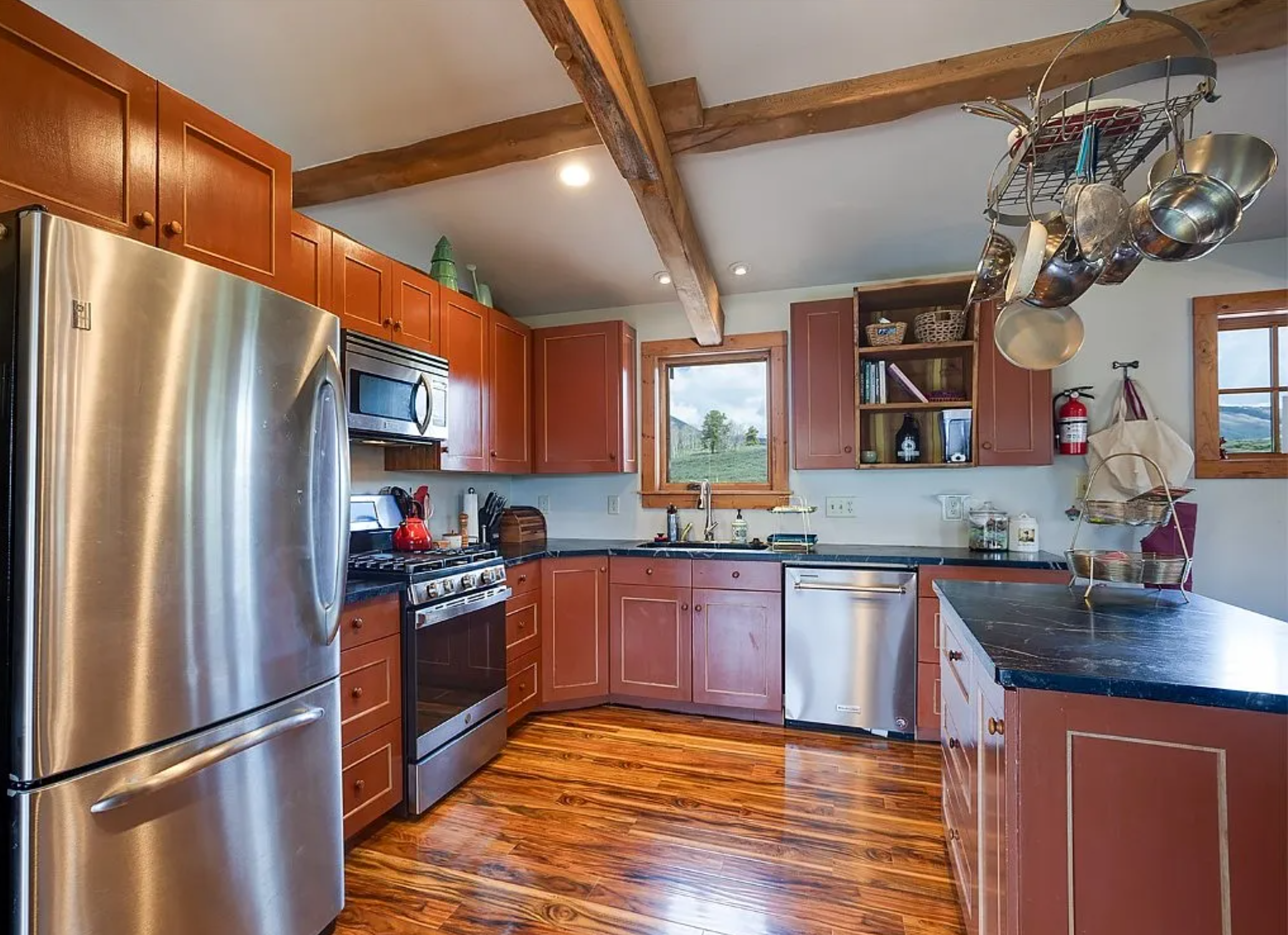 This is a warm and inviting kitchen featuring earth-toned cabinets and stainless steel appliances. Wood beams accent the ceiling, adding a rustic touch. The kitchen offers a functional layout with plenty of counter space and storage.