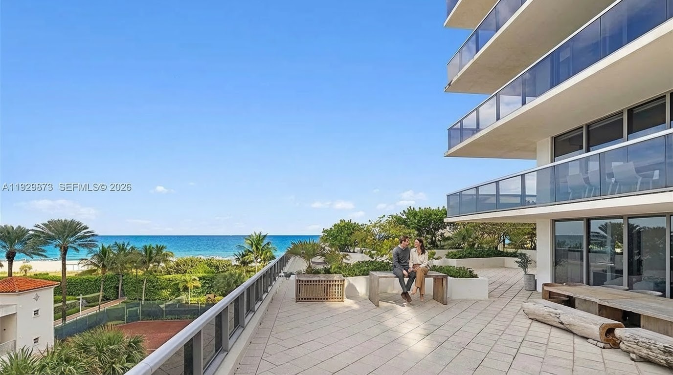 This image showcases a spacious balcony with stunning ocean views. A couple is seated on a bench, accentuating the relaxed atmosphere. The balcony features modern railings, neutral tiling, and elegant outdoor furniture, contributing to a luxurious and inviting ambiance, perfect for entertaining or relaxation.