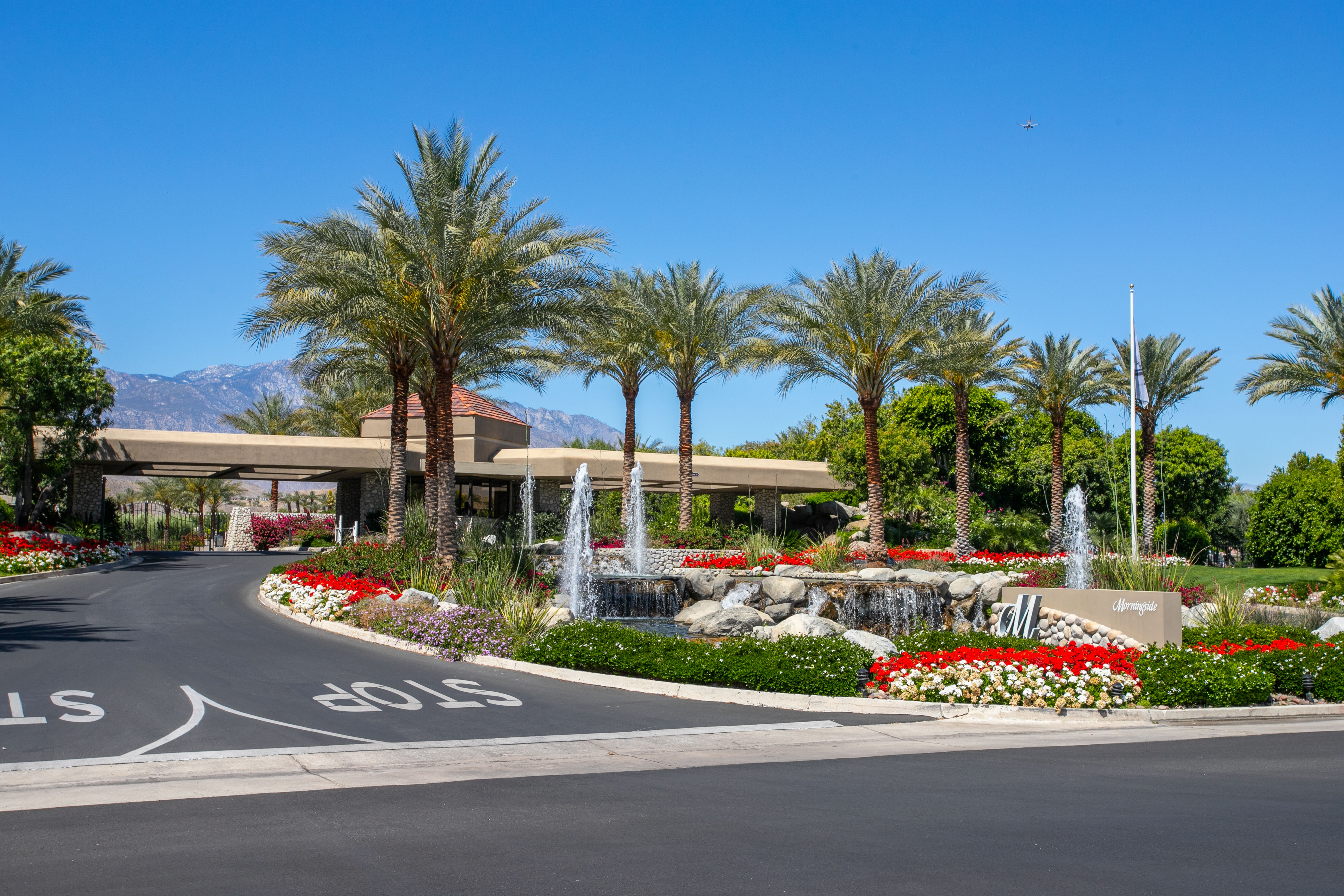This image showcases the impressive, well-manicured grand entrance of the Morningside community. It features a sweeping driveway leading to a gated entry, accented by lush landscaping, vibrant flower beds, and tiered water fountains. The scene exudes an upscale, resort-style atmosphere, highlighting the manicured curb appeal of this exclusive neighborhood.