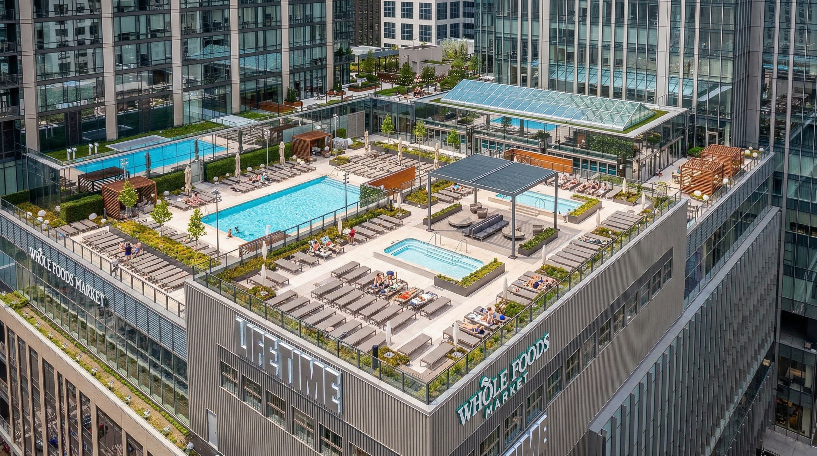 The image showcases an aerial view of a rooftop amenity space atop a building, featuring swimming pools, hot tubs, lounge areas with numerous sunbeds, and various seating arrangements. The building's facade is visible, incorporating signage for "LIFETIME" and "WHOLE FOODS MARKET", giving the impression of a luxurious urban living environment with convenient amenities and retail access.