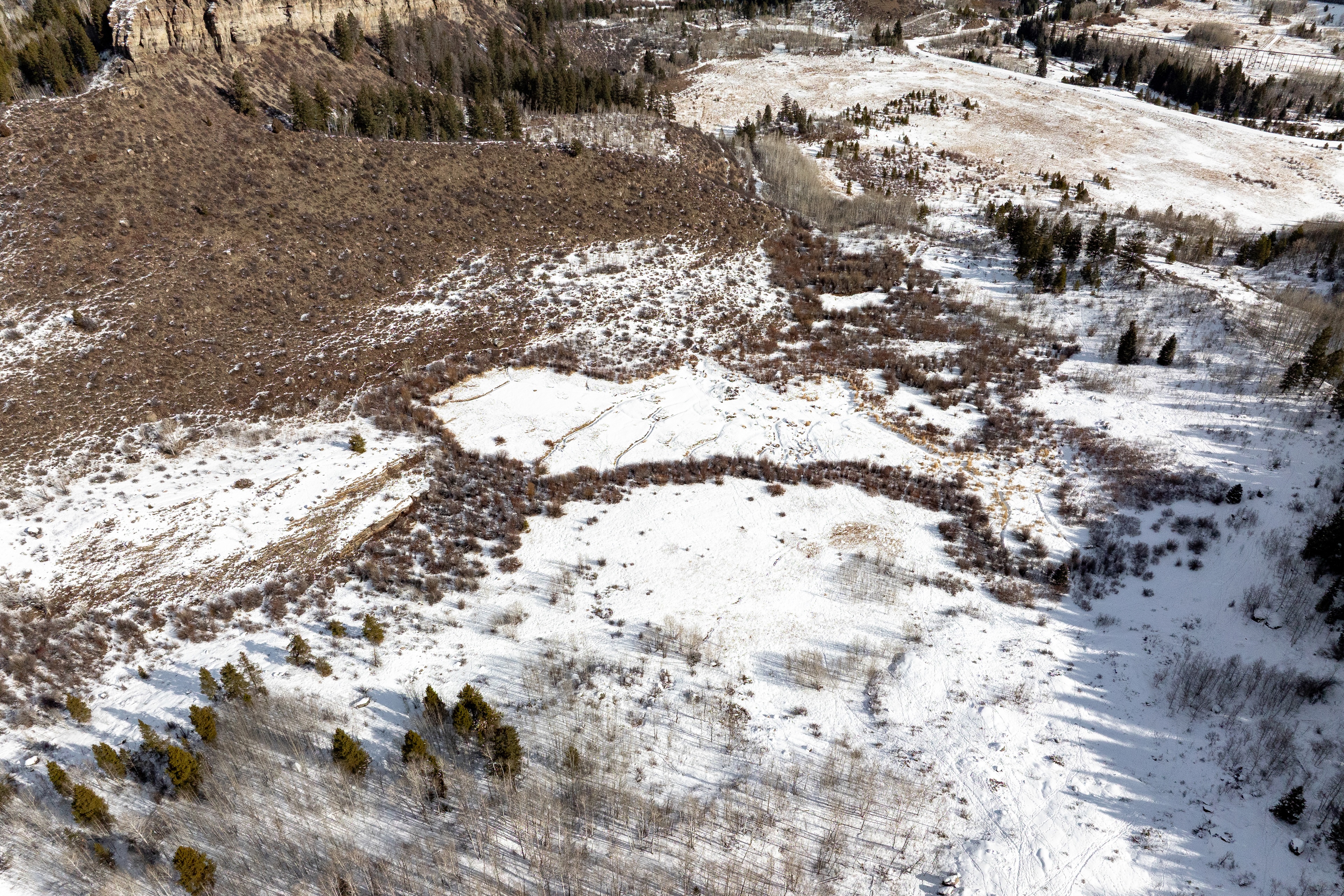 This aerial image showcases a serene, snow-covered landscape. The terrain varies from open meadows to wooded areas, creating a diverse natural environment. The image would appeal to buyers seeking properties with scenic views and outdoor recreational opportunities.
