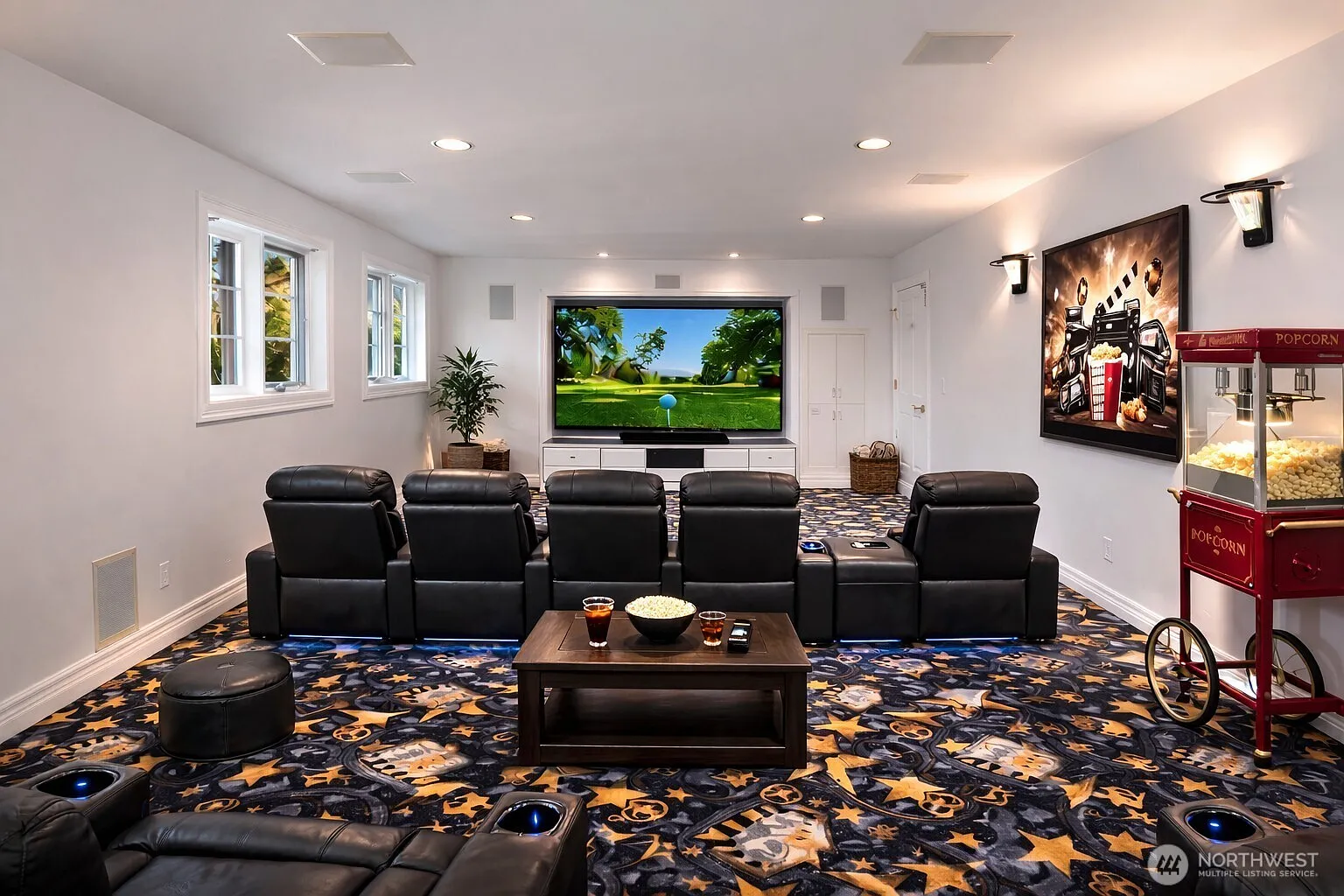 This is a well-appointed home theater in a basement. It features comfortable black leather reclining chairs, a large screen displaying a golf scene, and movie-themed decor like a popcorn machine and framed artwork. The patterned carpeting adds a playful touch to the space.