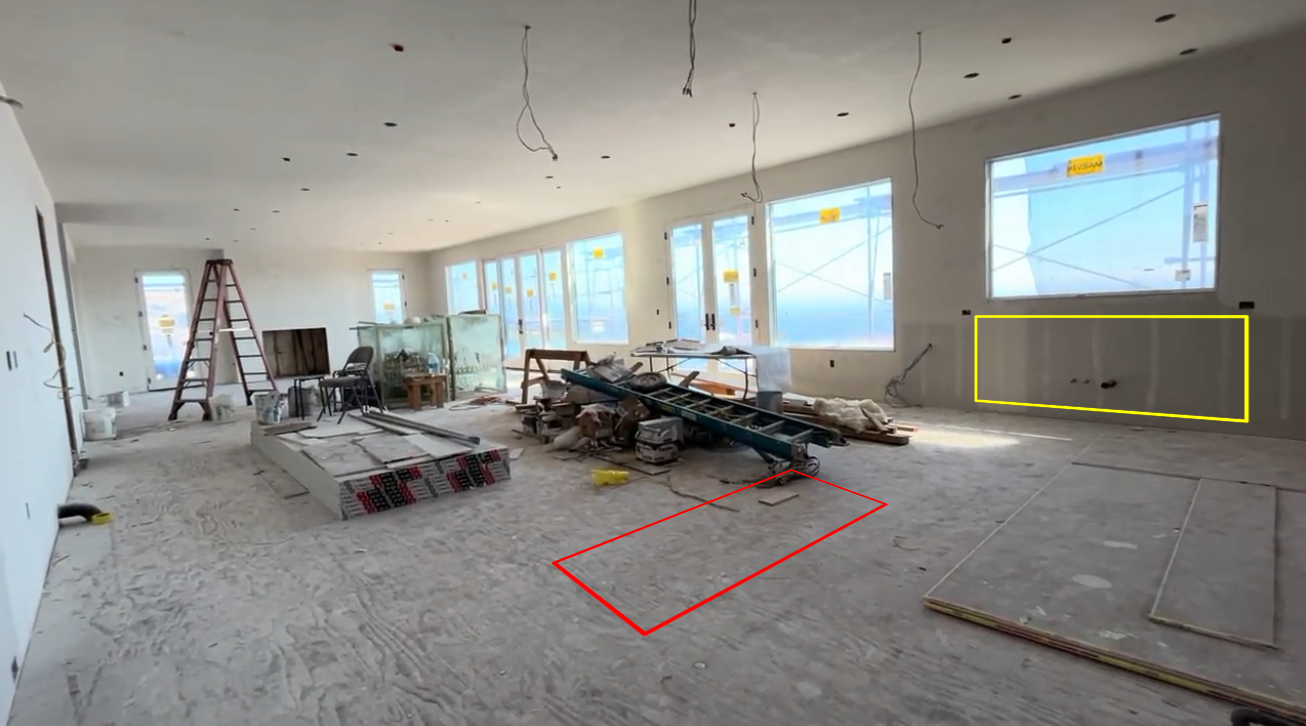 This is a large, open-concept living area currently under construction, featuring exposed drywall and wooden subflooring. The space is filled with construction materials, including tools and ladders, and has several large double glass doors that allow for abundant natural light. The layout offers plenty of potential for a spacious, modern great room design, with pre-installed plumbing outlets for future cabinetry or a wet bar.