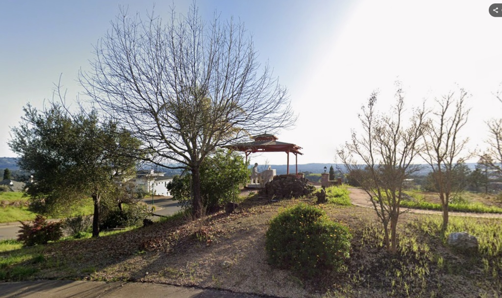 This outdoor space showcases a scenic, elevated garden area featuring a unique covered lookout structure with a statue. The landscaping includes mature trees, open greenspace, and expansive panoramic views of the surrounding hills, suggesting a peaceful environment for relaxation. It is a picturesque feature that emphasizes potential for an inviting and tranquil backyard retreat.