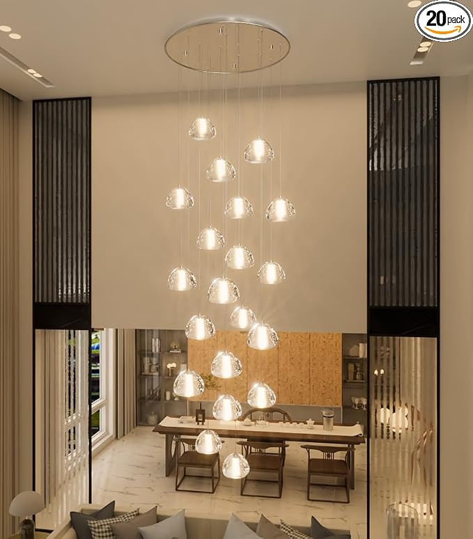 This spacious, double-height dining area is anchored by a dramatic, multi-tiered crystal pendant chandelier that serves as a stunning focal point. The room features a modern wooden dining table surrounded by comfortable chairs and is framed by elegant, floor-to-ceiling slatted room dividers. The open-concept design promotes an airy and sophisticated atmosphere, suitable for high-end entertaining.