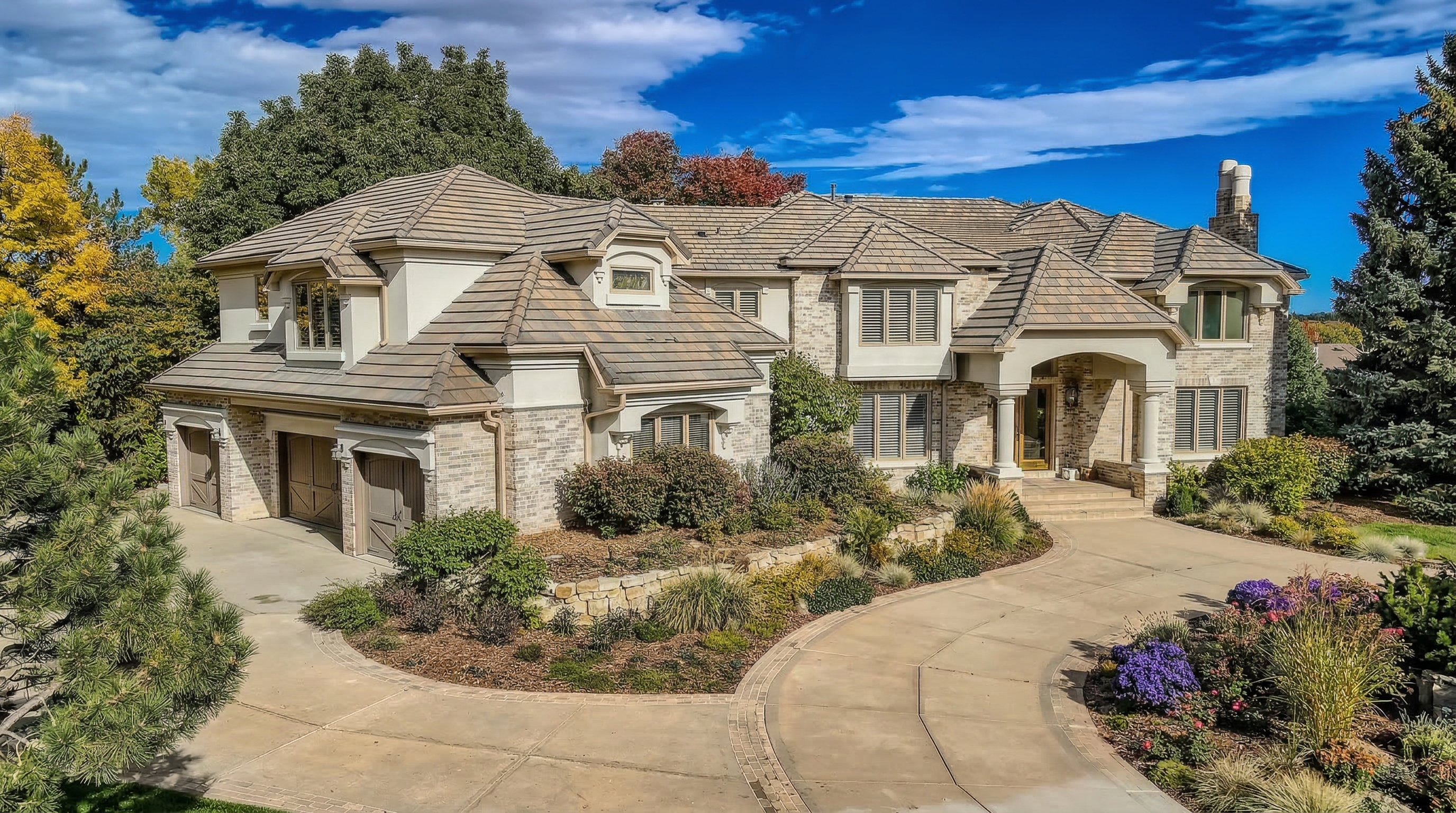 This elegant two-story estate features a sophisticated blend of light brick and stucco architecture with a prominent gabled roofline. The property boasts a spacious circular concrete driveway, professional landscaping, and multiple garage bays, creating a grand and inviting curb appeal. Its classic design and neutral color palette convey a sense of luxury and timeless comfort.