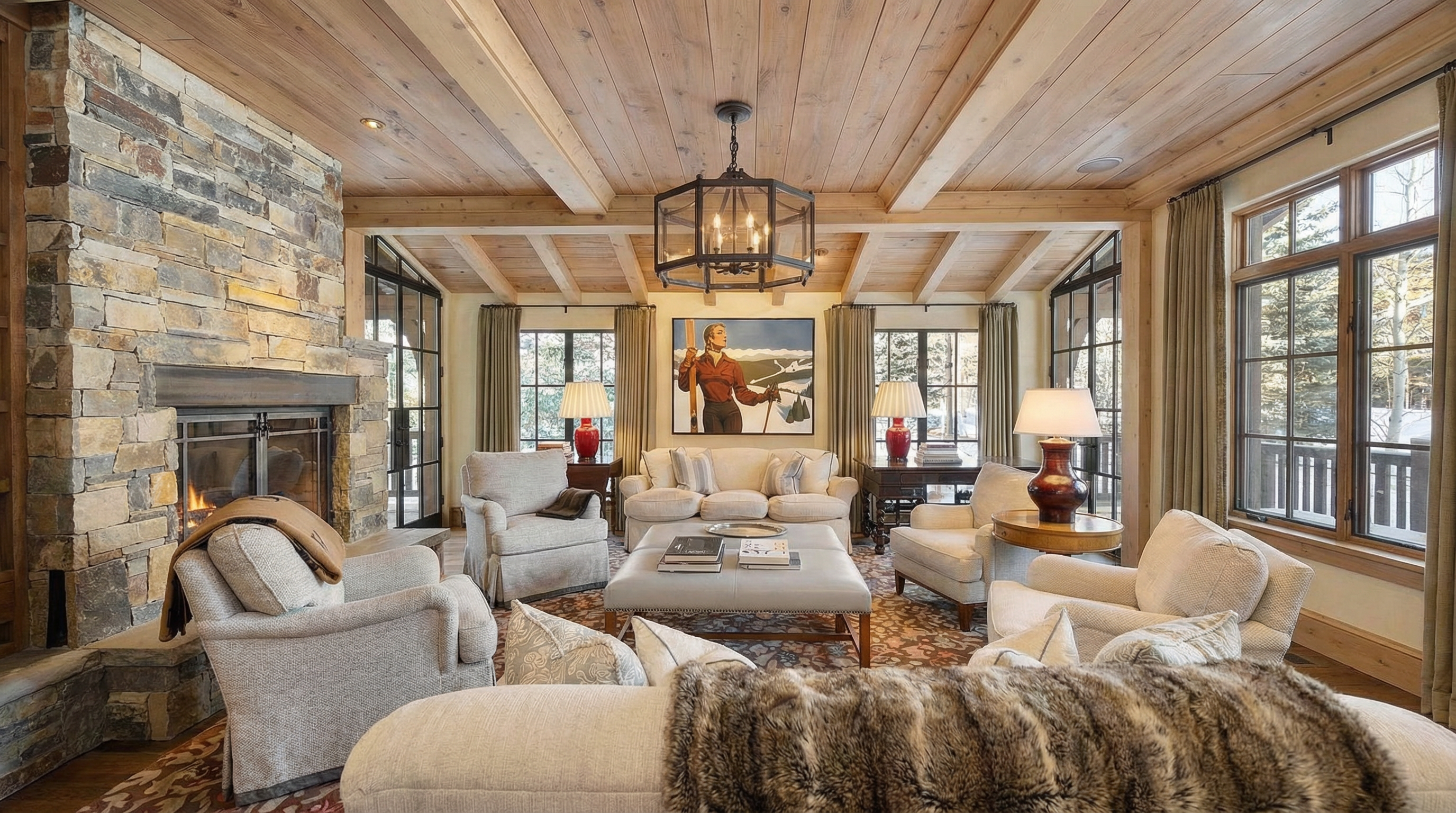 This inviting living room features a stone fireplace, beamed wooden ceiling, and comfortable seating arrangements. Large windows offer natural light and views of the outdoors. The space exudes a warm and cozy atmosphere, perfect for relaxation and gatherings.