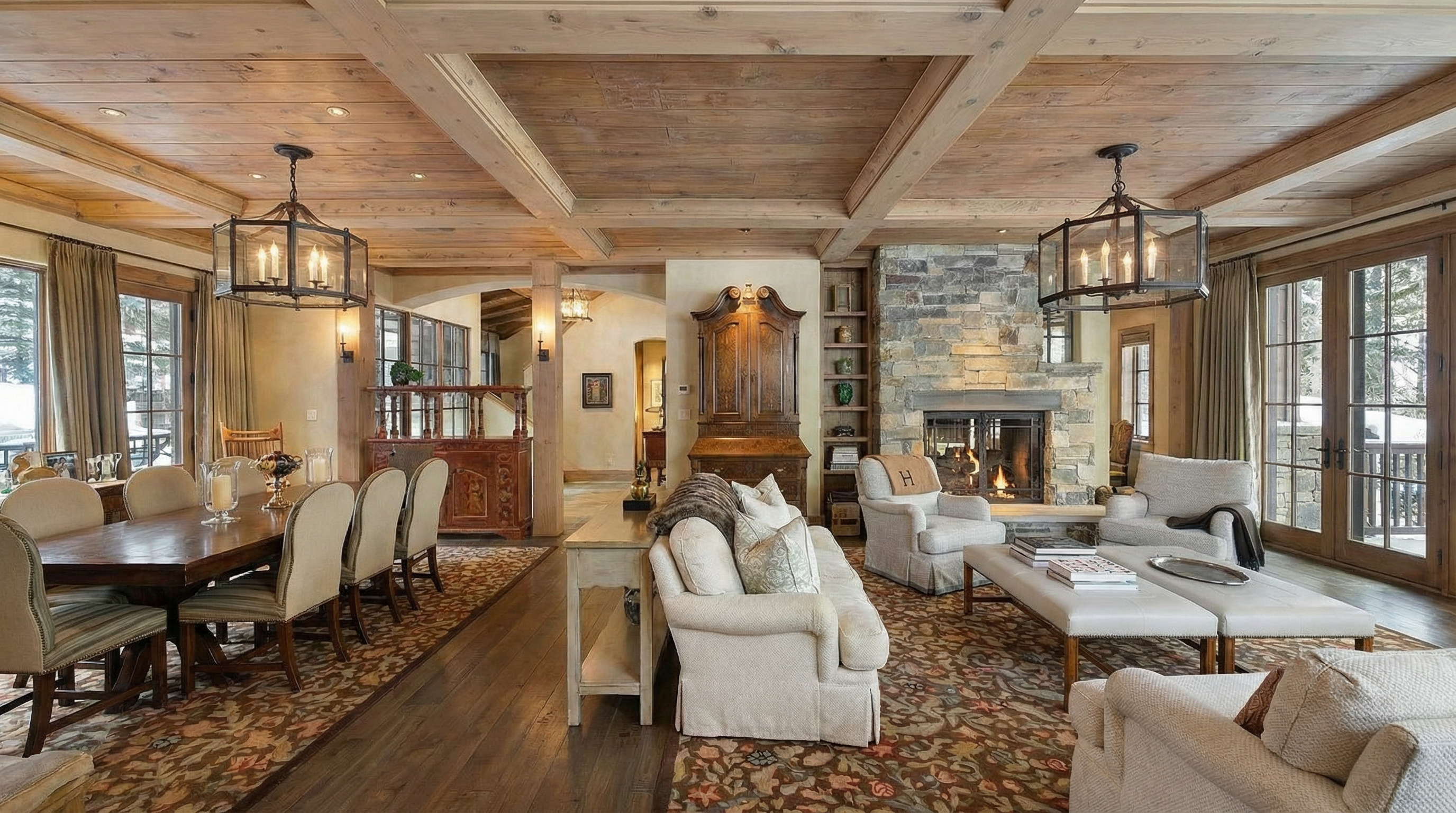 This is a well-lit living room with a rustic and luxurious style. Features include wood-beamed ceilings, a stone fireplace, and elegant furniture. The open layout creates a comfortable and inviting atmosphere, perfect for family gatherings or entertaining guests.