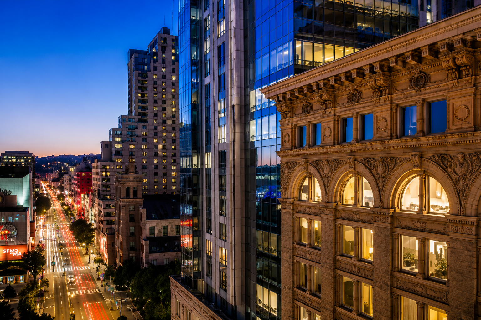 This stunning cityscape photograph captures a juxtaposition of historic architecture and modern glass towers against a clear evening sky. The frame features a detailed, ornate stone building in the immediate foreground, complemented by a busy urban street with light trails from moving traffic. The overall impression is one of sophistication and vibrant city living in a high-density downtown area.