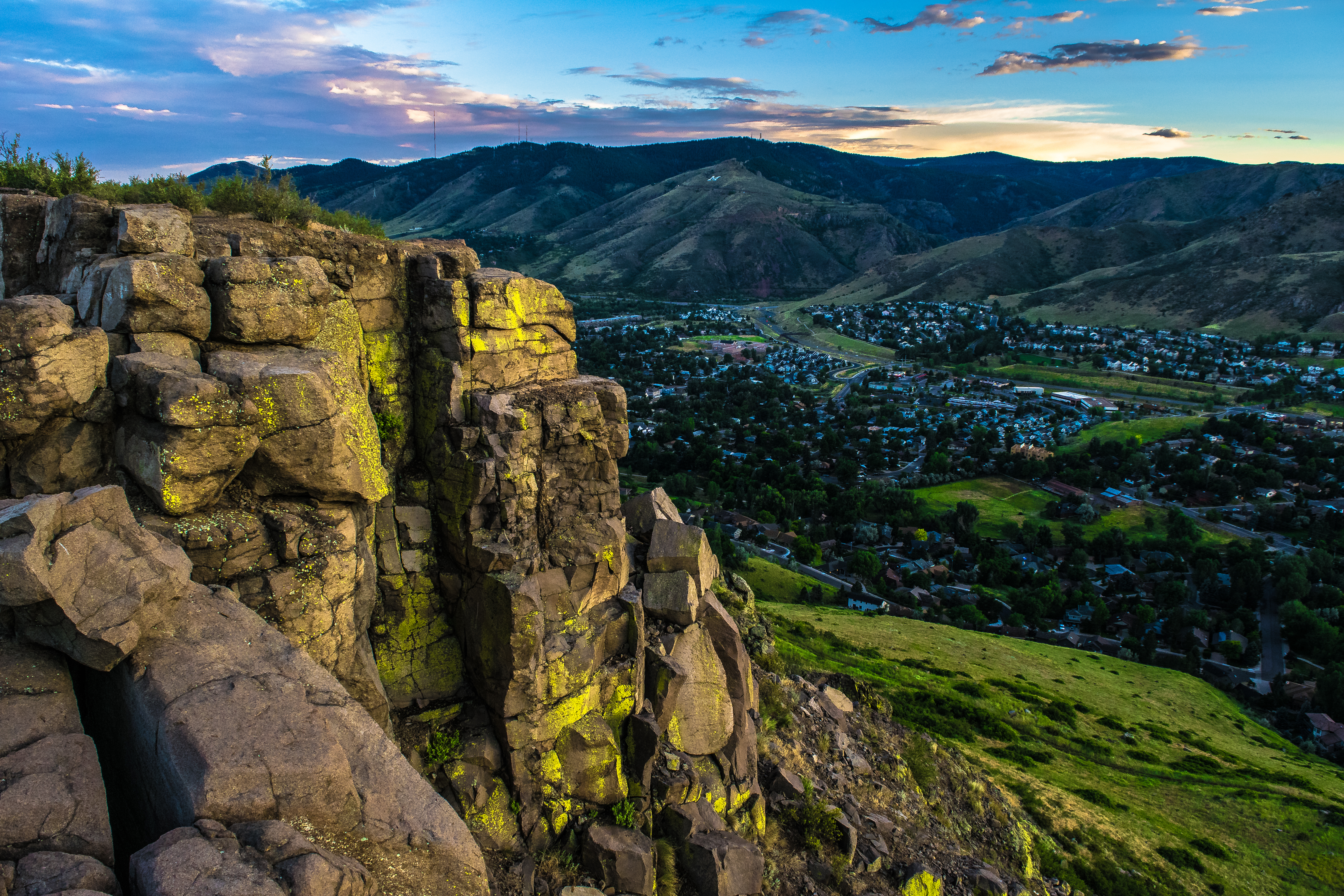 This aerial view captures a picturesque scene of a town nestled in a valley surrounded by mountains. The composition features dramatic rock formations in the foreground and a vibrant daytime sky. This image would be excellent for showcasing the natural beauty and prime location of real estate in the region.