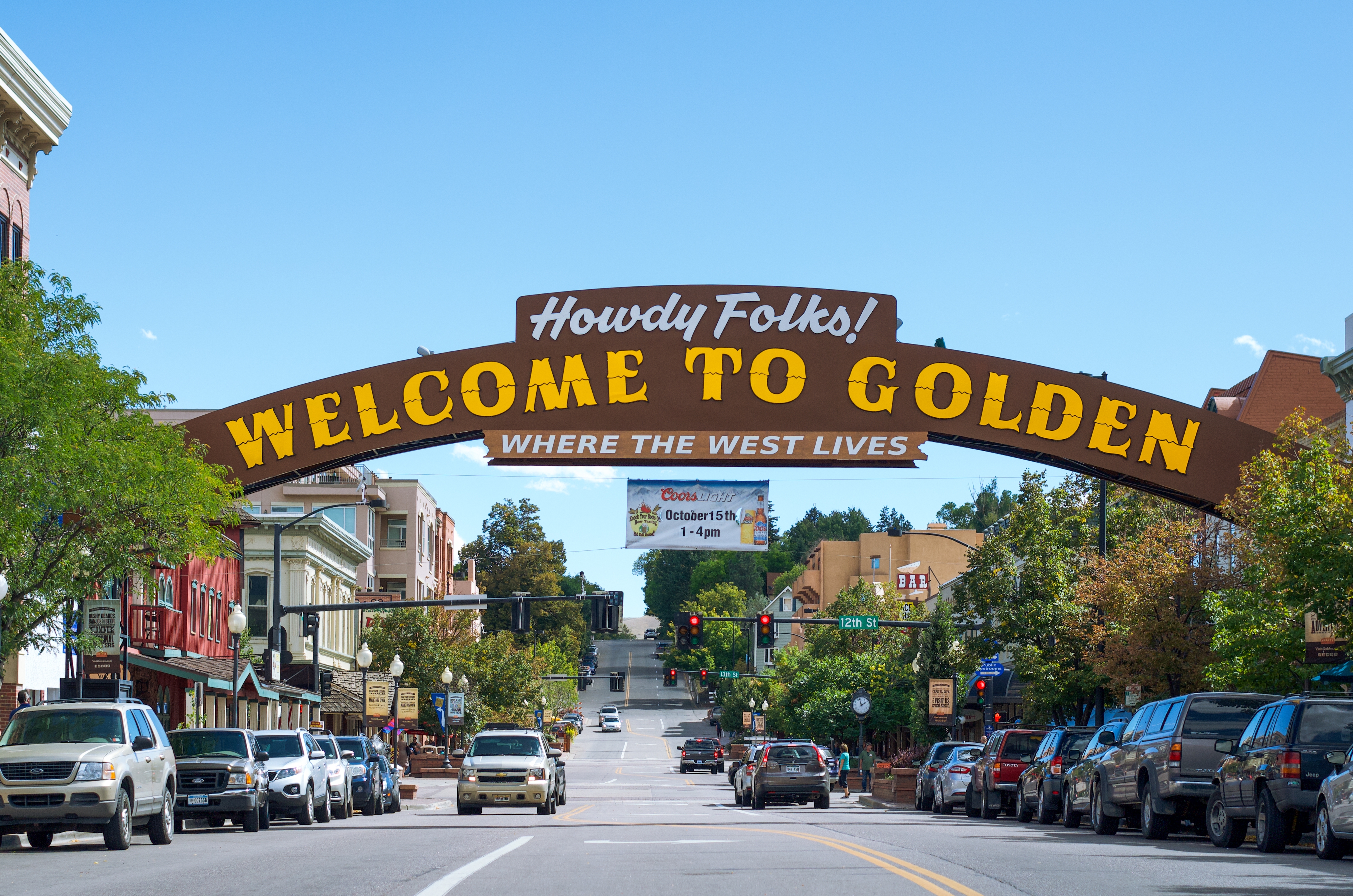 This image showcases the entrance to a town, marked by a "Welcome to Golden" sign arching over the main street. The street is lined with parked cars and buildings, giving a vibrant and historic feel. The scene suggests a charming downtown area, ideal for attracting residents and visitors.