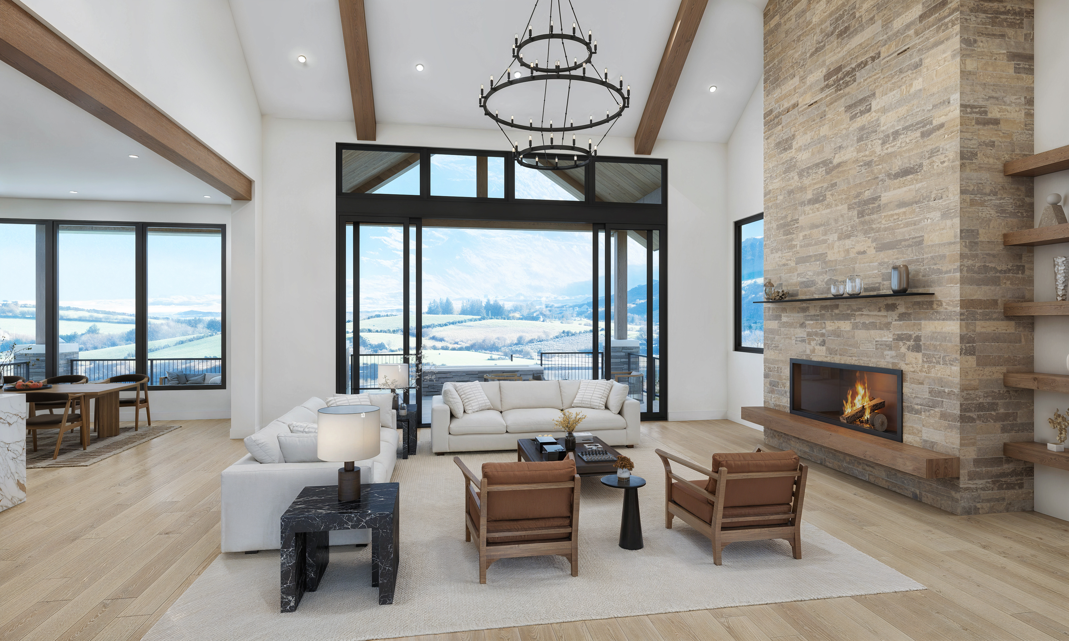 This expansive living room showcases modern design with vaulted ceilings and exposed wooden beams. Large windows offer stunning views of the landscape, while a stone fireplace adds a touch of rustic charm. The room features two couches, two armchairs, and a chic chandelier, creating an inviting and luxurious atmosphere.