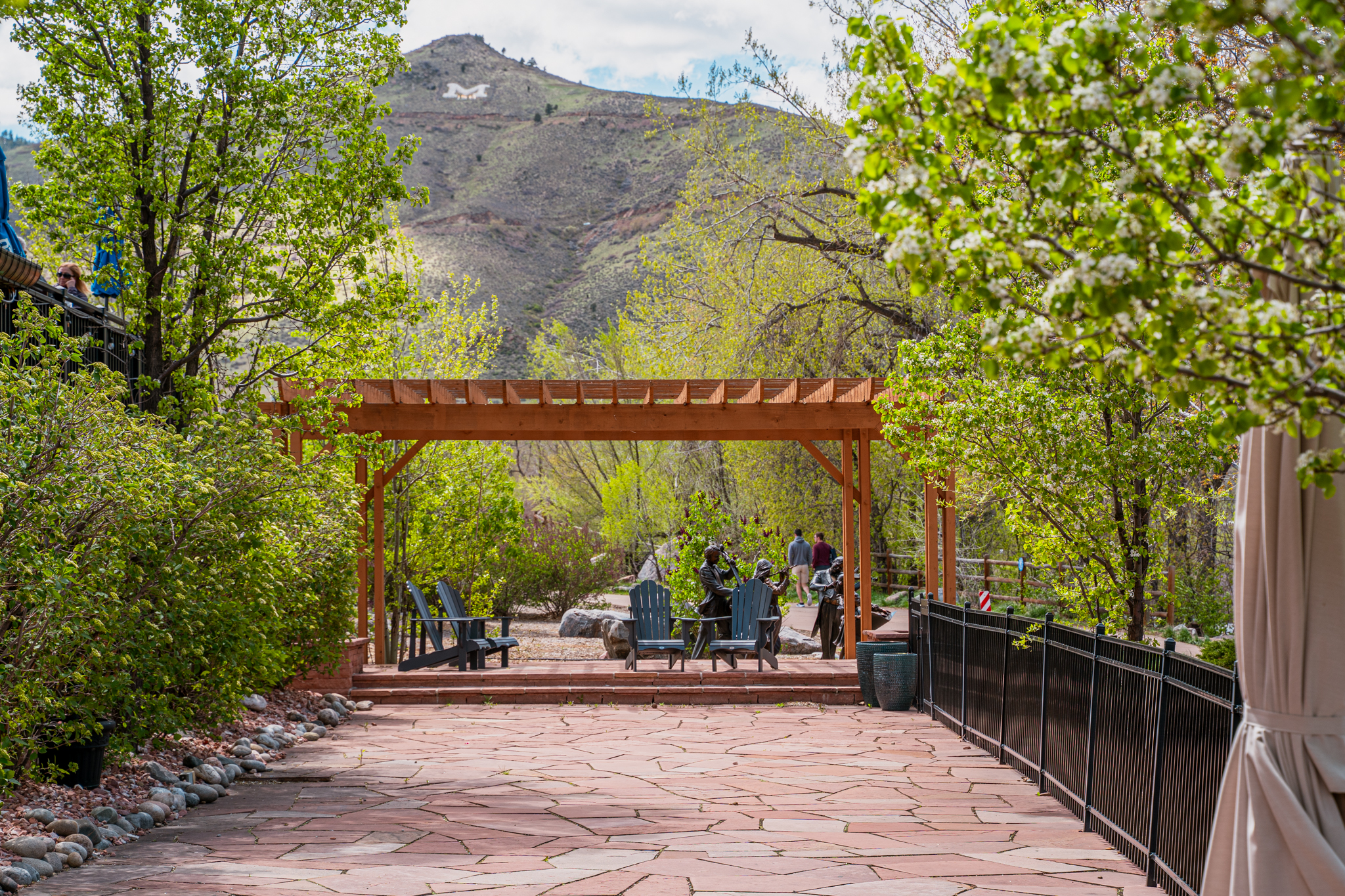 This outdoor space showcases a beautiful stone patio with a wooden pergola, creating an inviting atmosphere. Lush greenery surrounds the area, complemented by the mountain view in the background, making it an ideal setting for relaxation or entertainment. The carefully designed landscaping and hardscaping enhance the property's appeal and offer a serene outdoor living experience.
