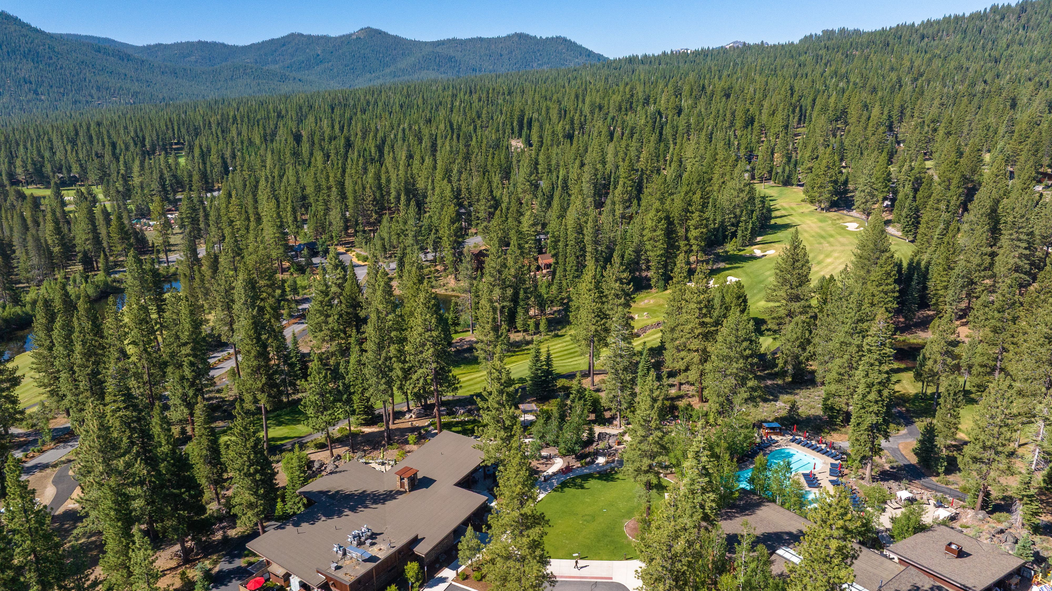 This aerial view showcases a luxurious property nestled amidst a lush forest setting, likely near a golf course. The focal point is a well-maintained swimming pool area, along with the building's roof structure. The surrounding landscape provides a sense of privacy and exclusivity, making it appear to be a desirable location.